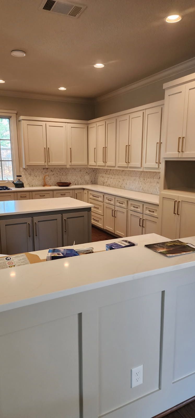 A large, bright kitchen with white cabinets, countertops, and a grey island.