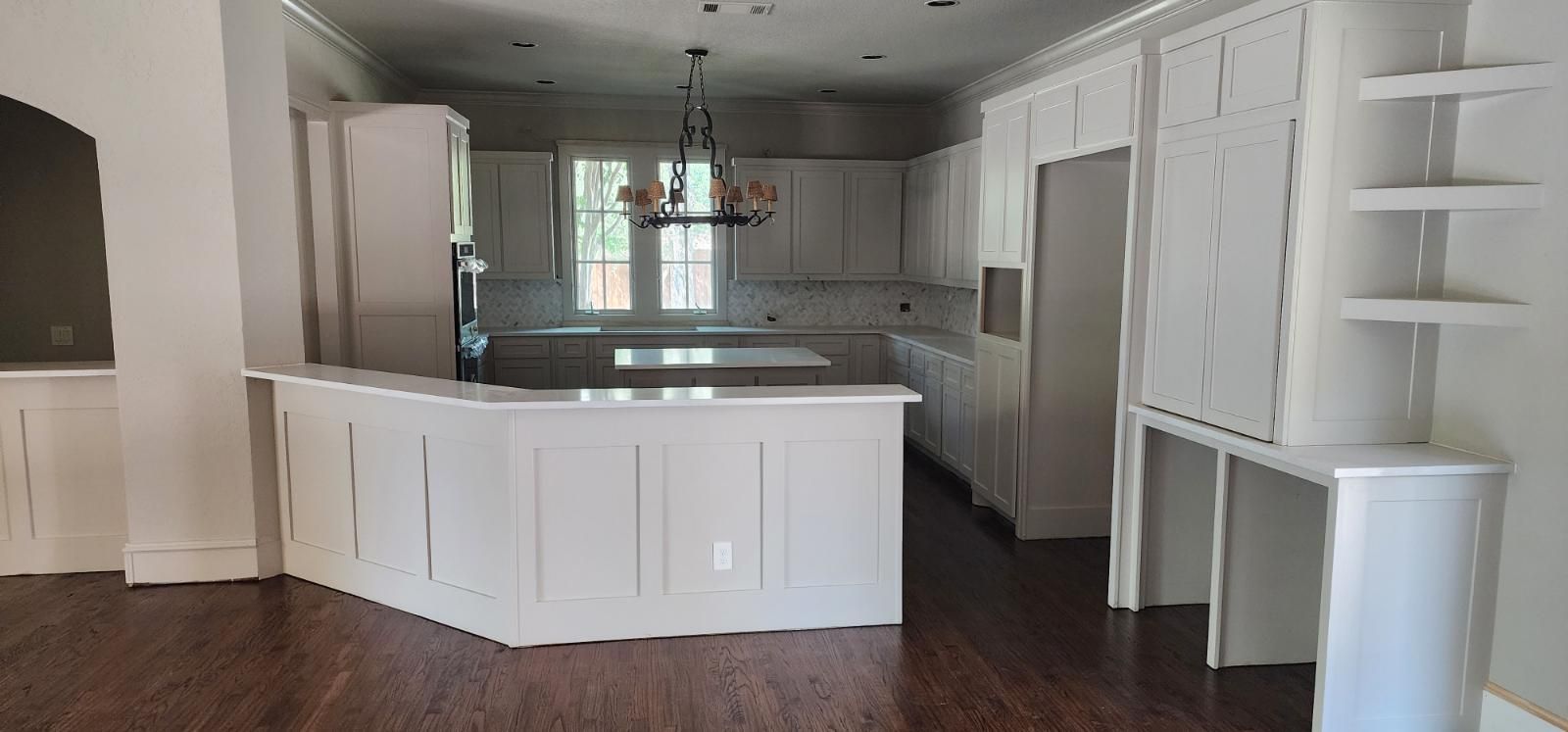 White kitchen with island, cabinets, and a chandelier over the island in a bright room.