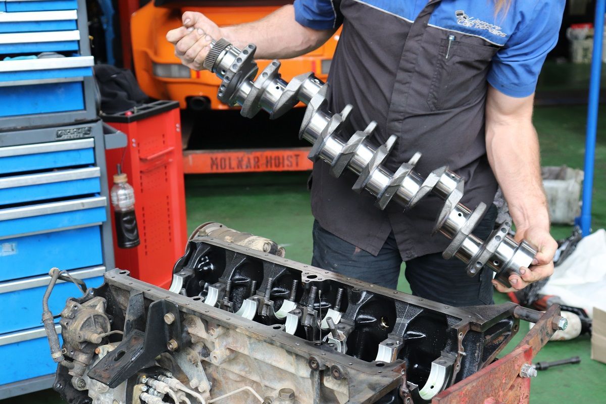 Mechanic Holding Shiny Crankshaft Next To Engine Block — Ballina Car Centre in Ballina, NSW