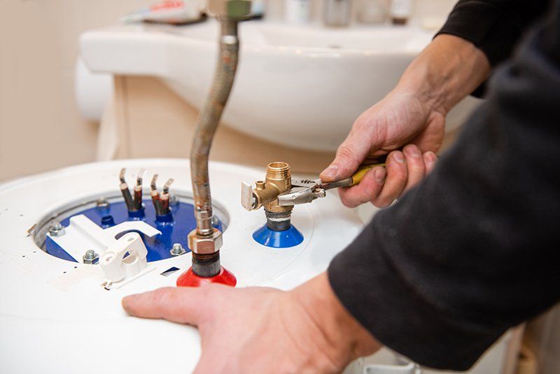 Plumbing technician tightens fitting on tanked water heater unit