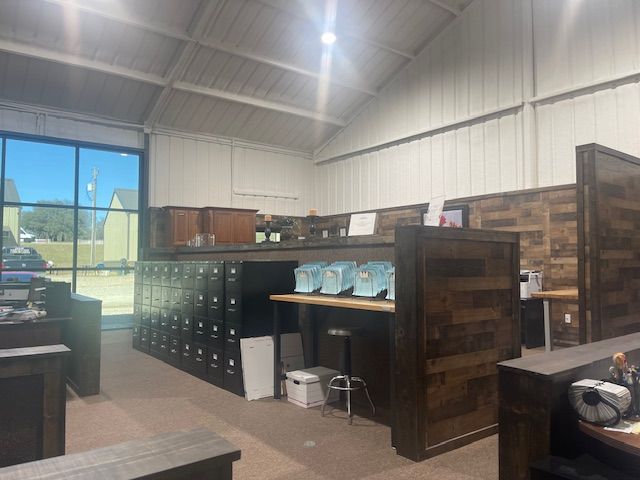 A rustic interior office with a long dark wooden desk, rows of black filing cabinets, and pale blue modular cubicles.