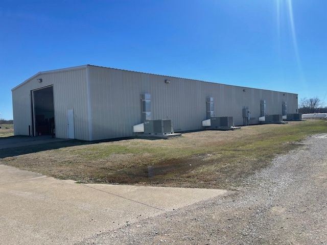 A large, beige metal warehouse building under a clear blue sky, with multiple wall-mounted HVAC units on the side.