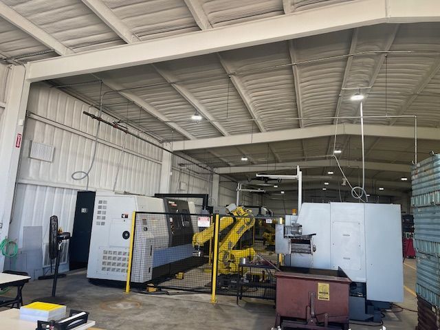 A yellow industrial robot stands between two metal CNC machines in a spacious factory workshop.