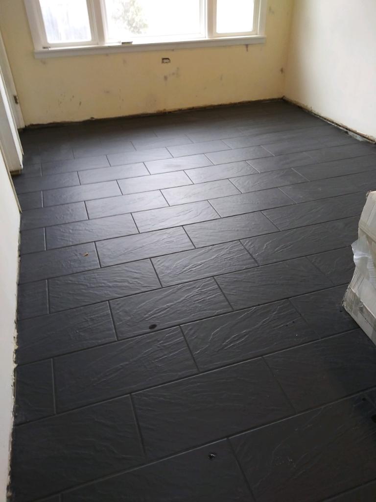 new dark tile floor installation with matte finish for empty family room renovation.