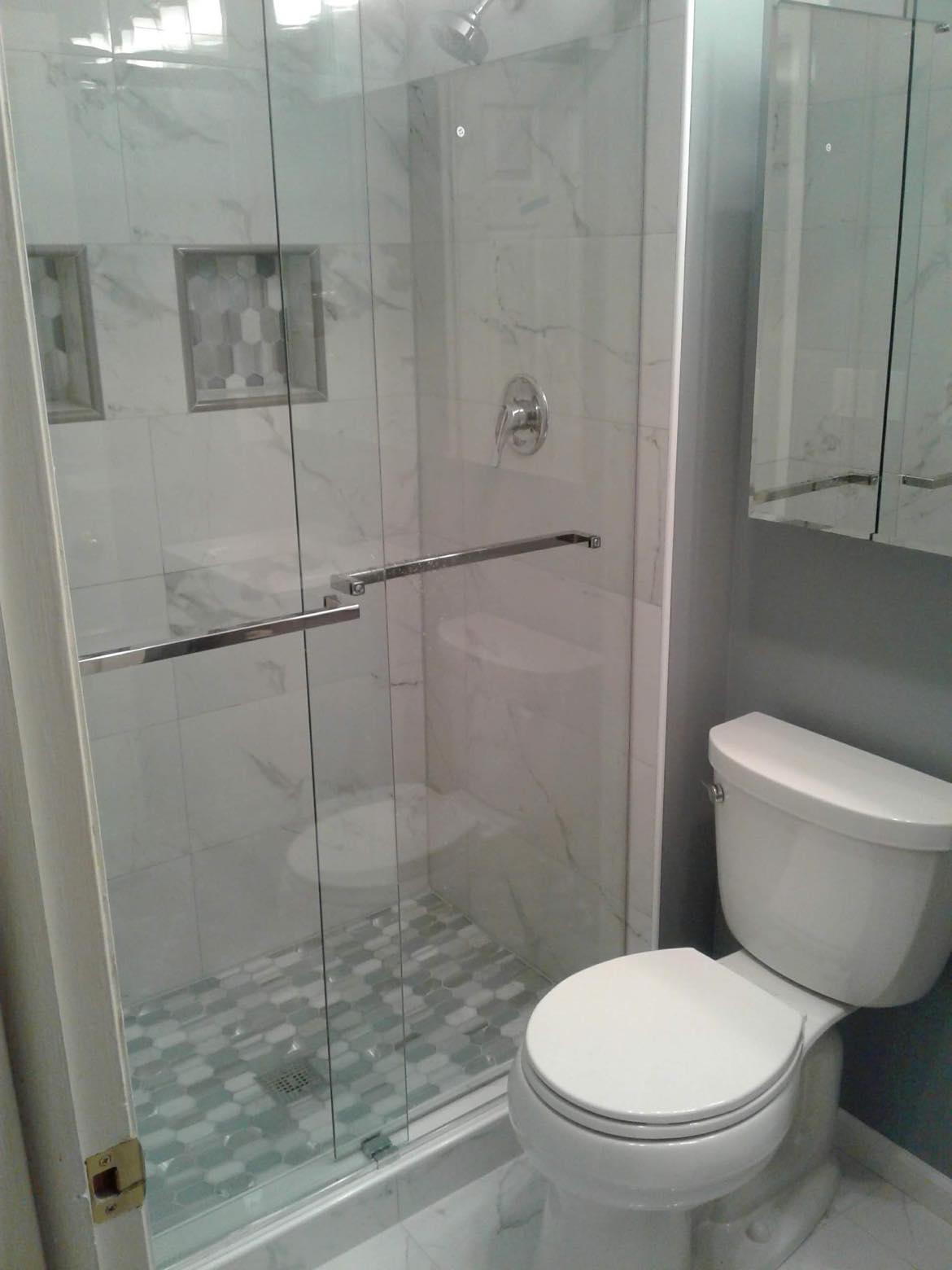 Standing shower stall remodeling with glass shower doors,  pattern floor and wall tiling, new toilet, and granite quartz tiling floors.