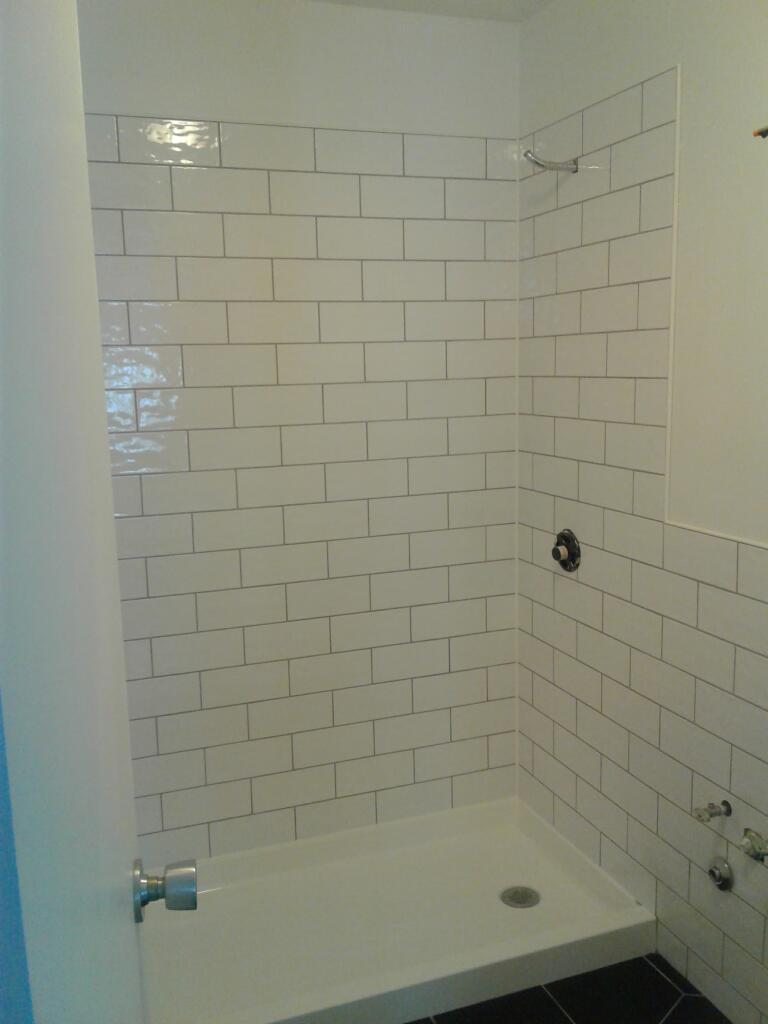 new all white brick style tiling backdrop for shower stall, all new shower base and black bathroom floor tiling for new bathroom renovation.