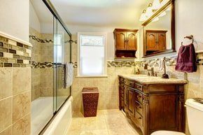classic bathroom renovation with tile design on both walls and flooring. glass door shower with tile finish . big mirror over bathroom sink.