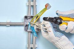 multi color wiring for a light switch being cut by an electrician handyman wearing gloves and snipping the wire with wire clippers.