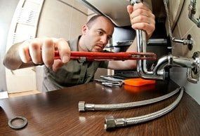 handyman plumber fixing metal drain pipe under sink in the kitchen.