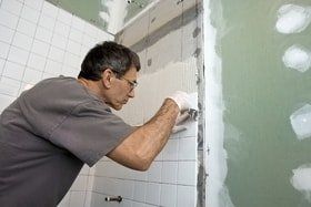 male handyman working on and fixing bathroom tile with green painted walls. Replacing tiles in the bathroom with white ceramic 6in bathroom tiles.