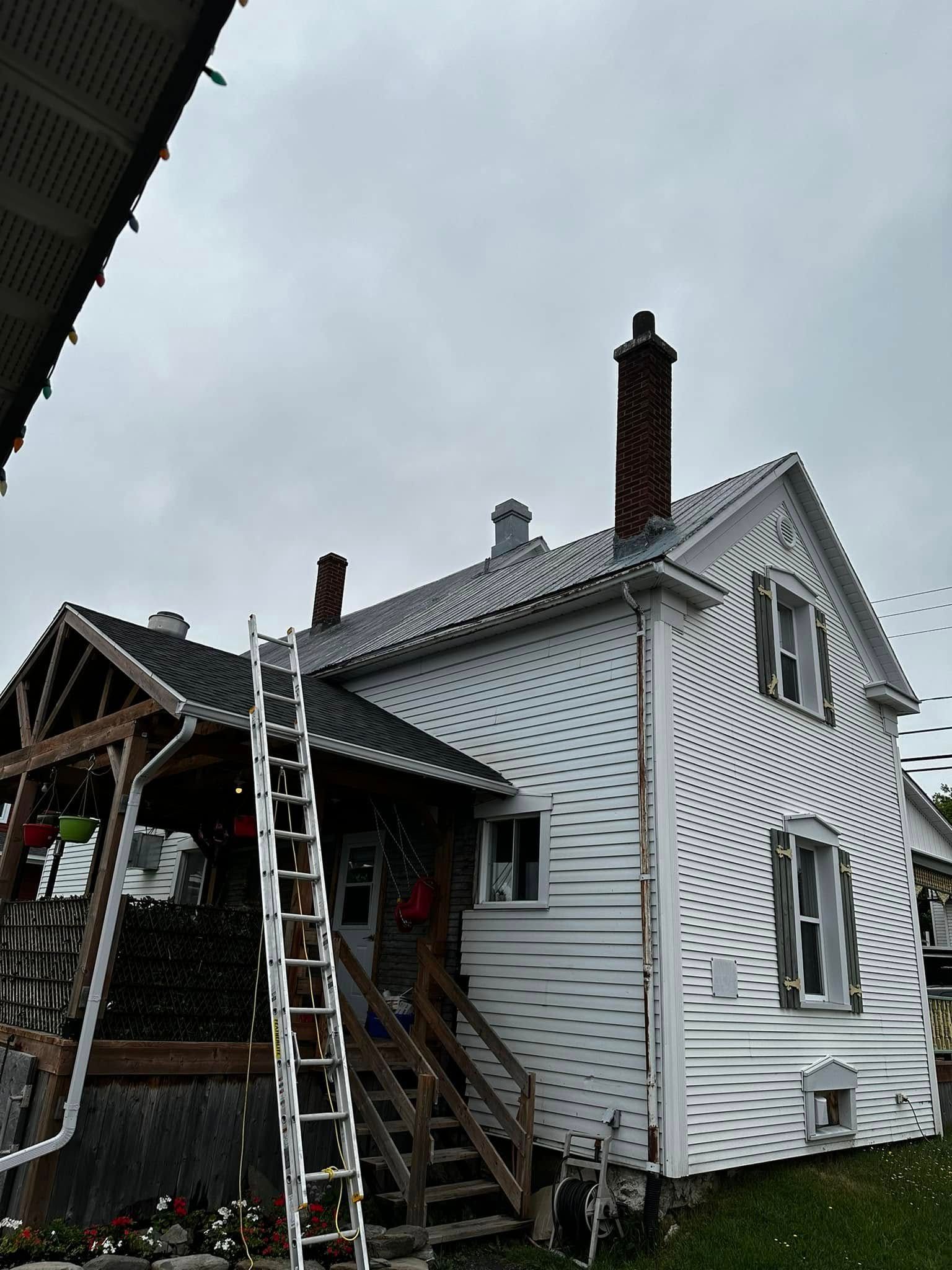 Maison blanche avec toit endommagé, échelles et débris à côté d'un porche couvert après les dégâts causés par la tempête