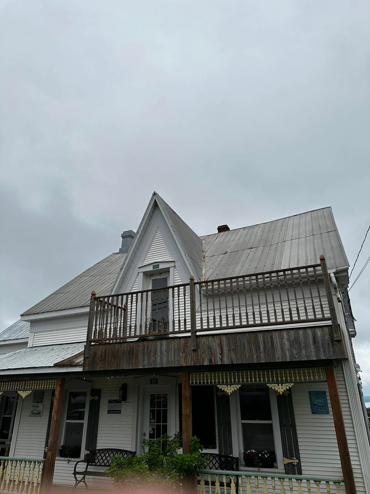 Maison blanche à deux étages avec un toit pentu et un balcon à l'avant sous un ciel nuageux