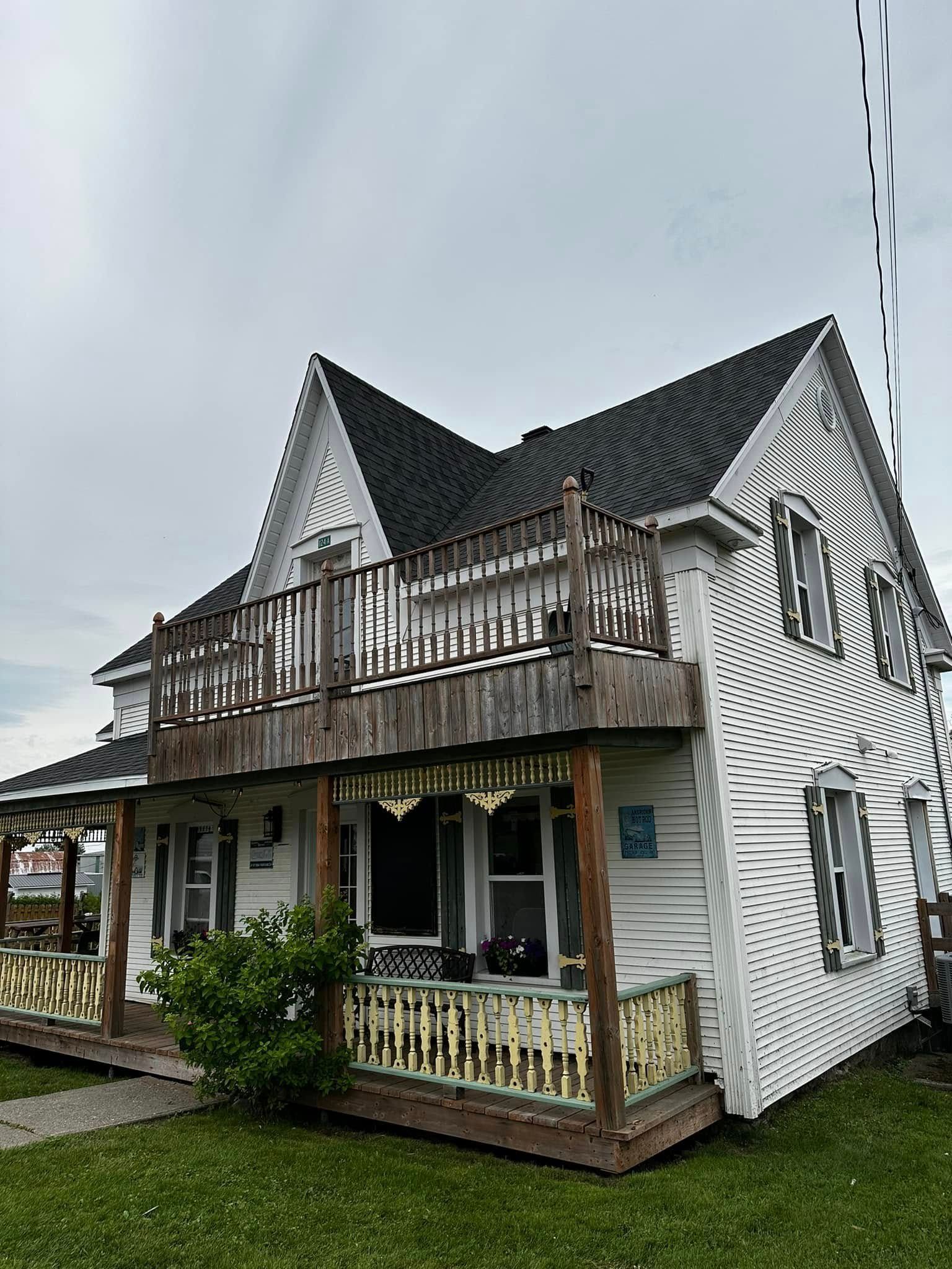Maison blanche de style victorien avec toit noir, façade rayée et véranda enveloppante sur une pelouse.