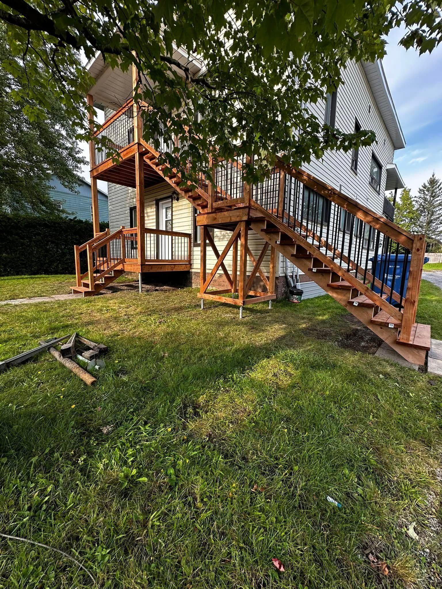 Escalier extérieur en bois et terrasse attenante à la maison, avec pelouse et arbres dans le jardin.