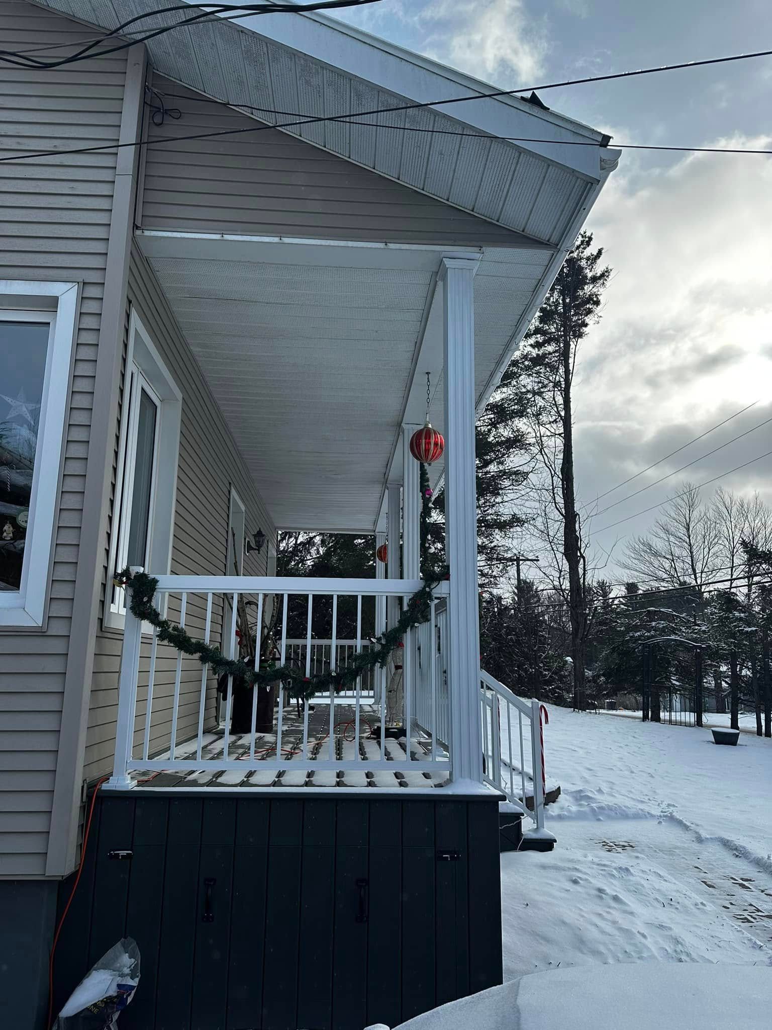 Porche enneigé d'une maison ornée d'une couronne rouge, avec un paysage hivernal au-delà.