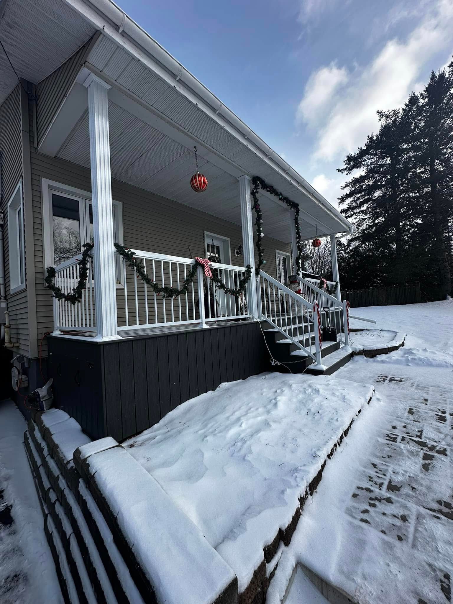 Porche enneigé d'une maison orné d'une guirlande de Noël et d'une décoration rouge suspendue par une journée d'hiver