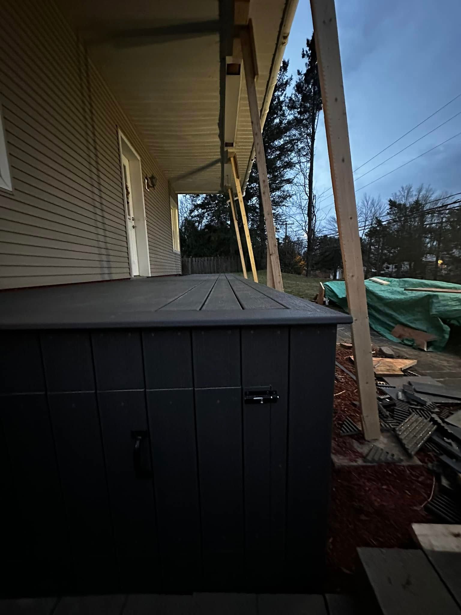 Véranda couverte avec des armoires de rangement sombres, jouxtant une maison et donnant sur un jardin au crépuscule.