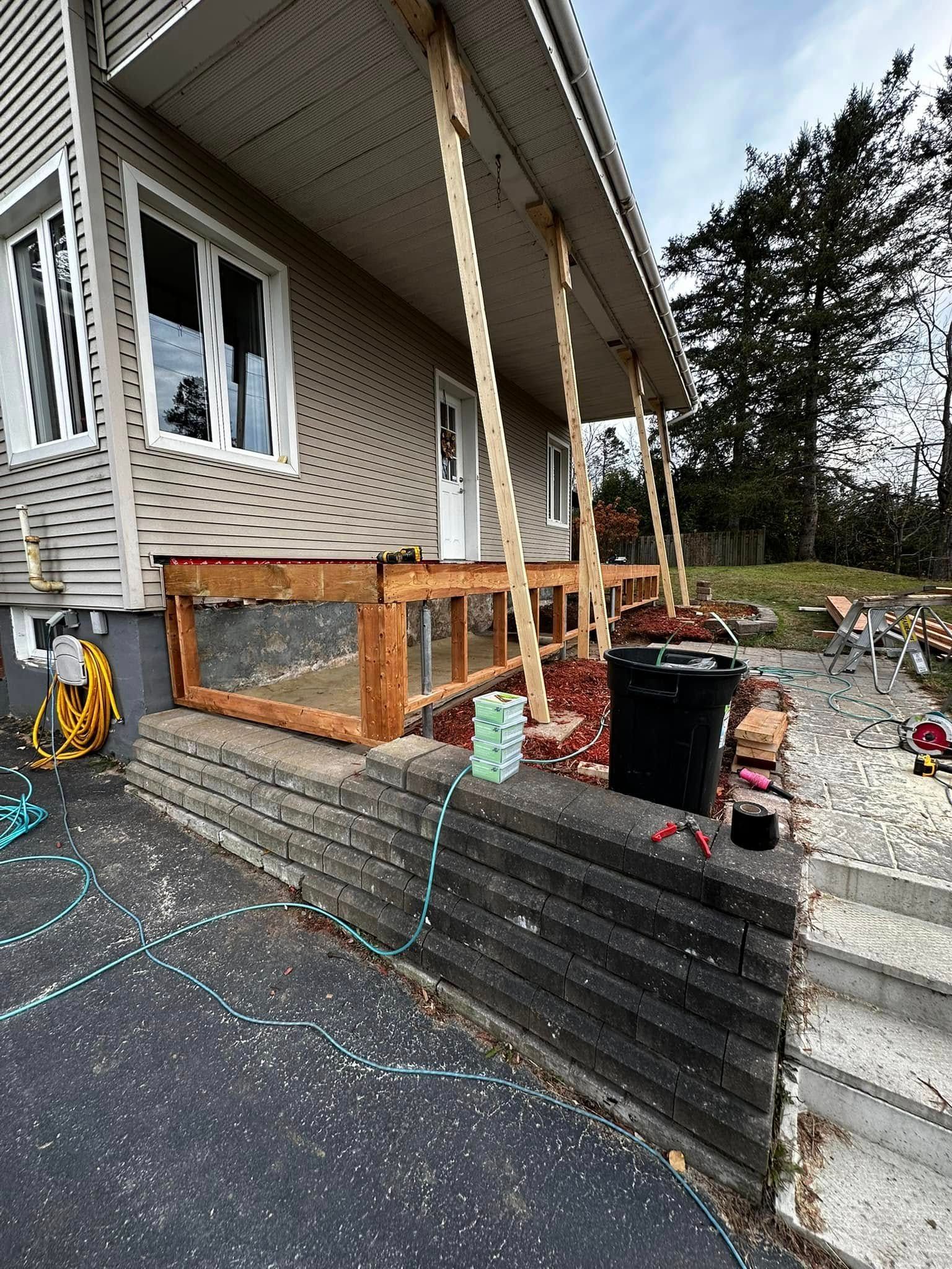 Porche d'entrée avec rampe temporaire noire, poteaux en bois et outils à côté de l'extérieur d'une maison