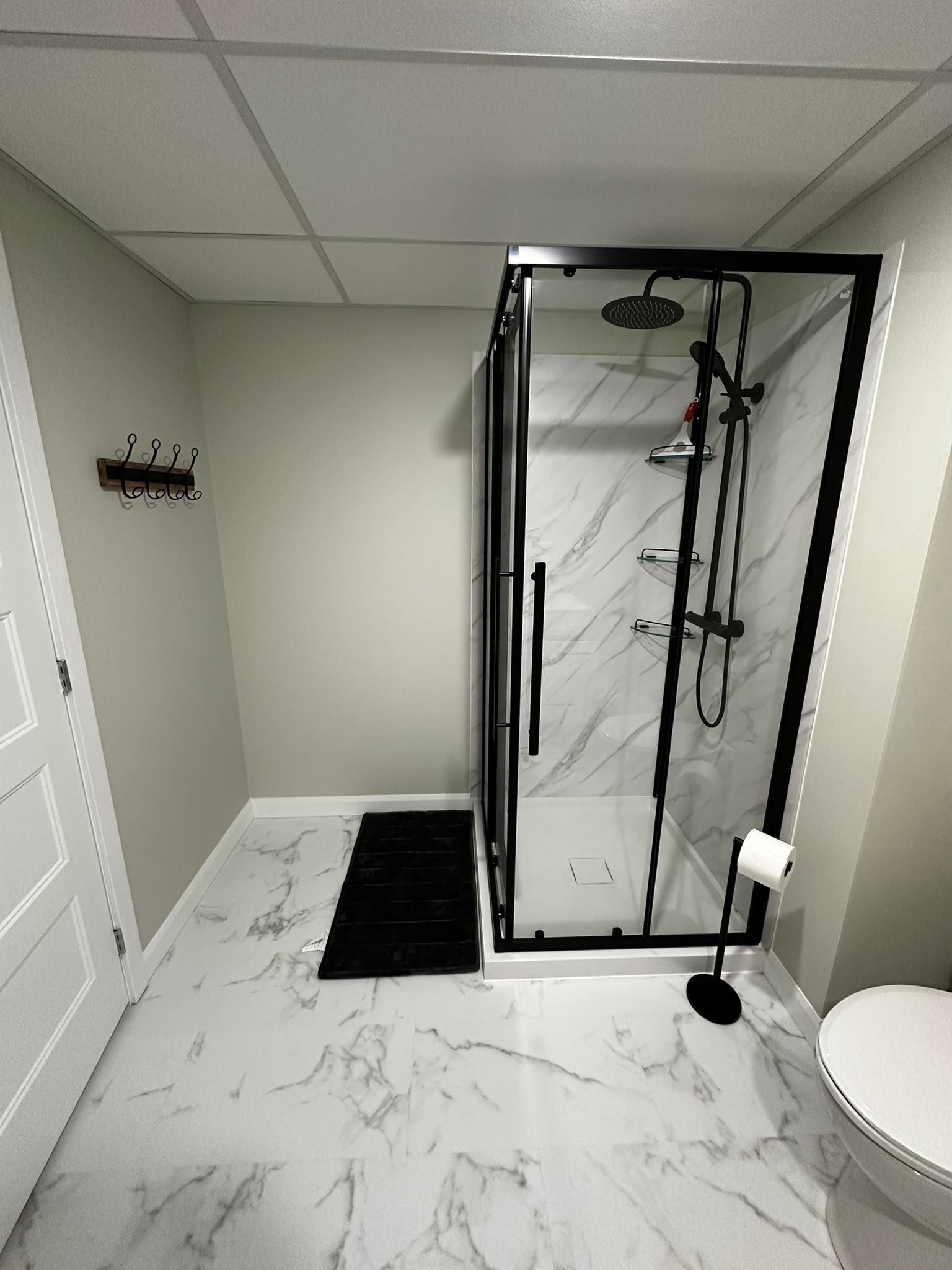 Salle de bains moderne avec douche à l'italienne, sol en marbre, touches de noir et toilettes partiellement visibles.