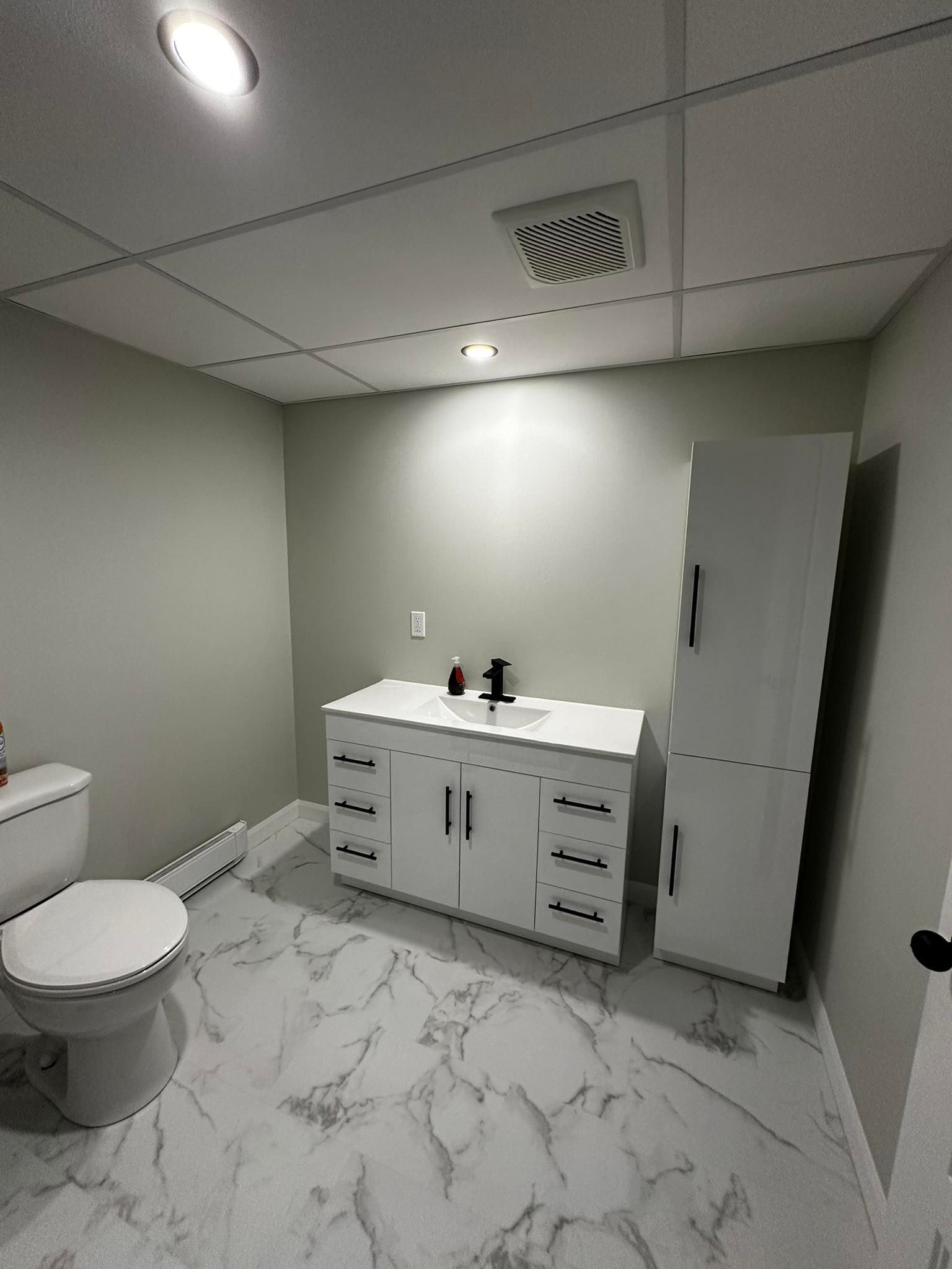 Salle de bains moderne avec sol en marbre, double vasque, toilettes et armoire haute sous éclairage encastré au plafond.