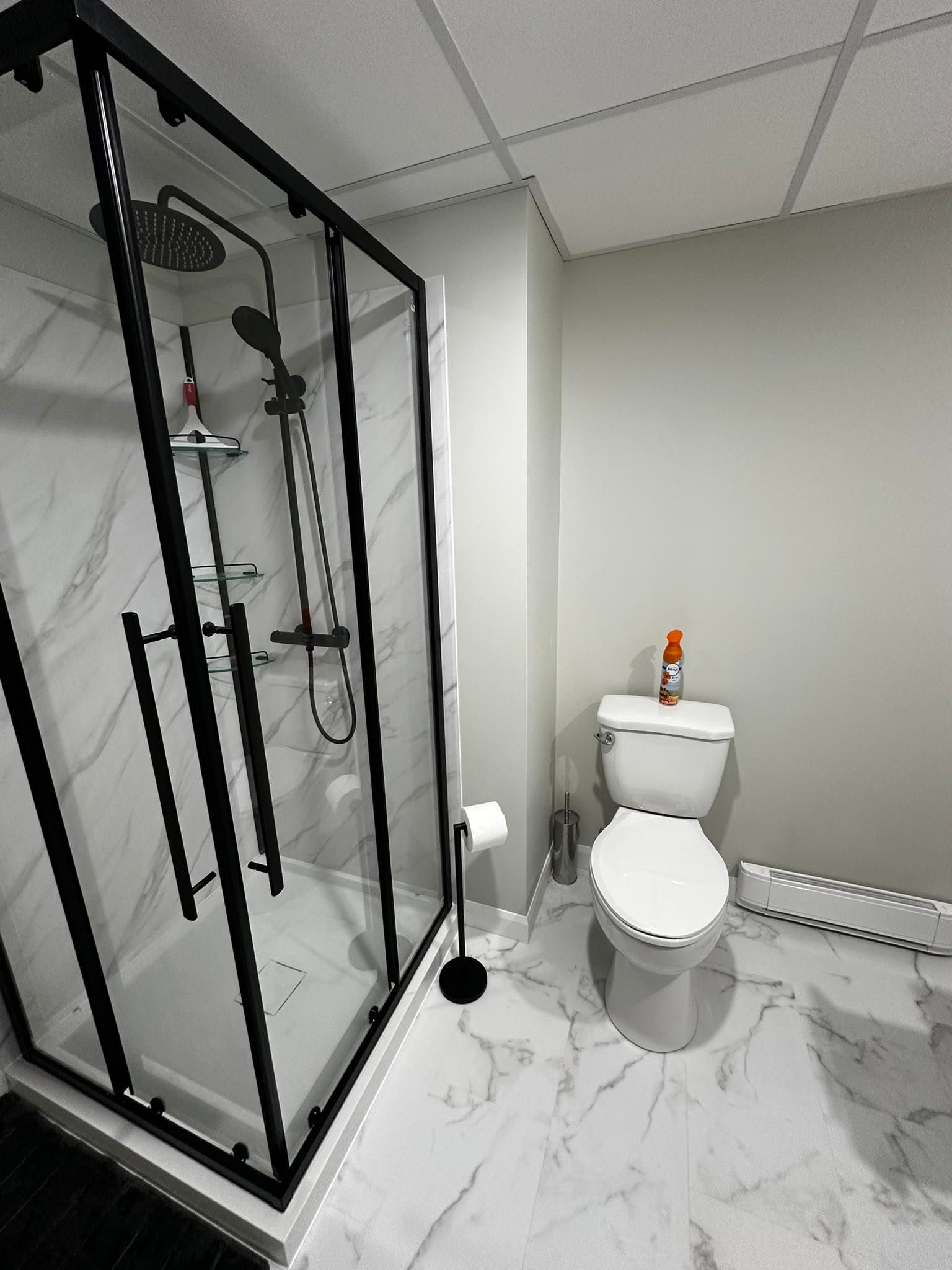 Salle de bains moderne avec douche en verre, toilettes blanches, sol en marbre et murs gris.