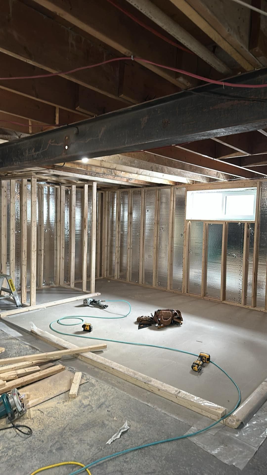 Sous-sol non aménagé avec charpente apparente, poutres de plafond, isolation et outils de construction au sol.