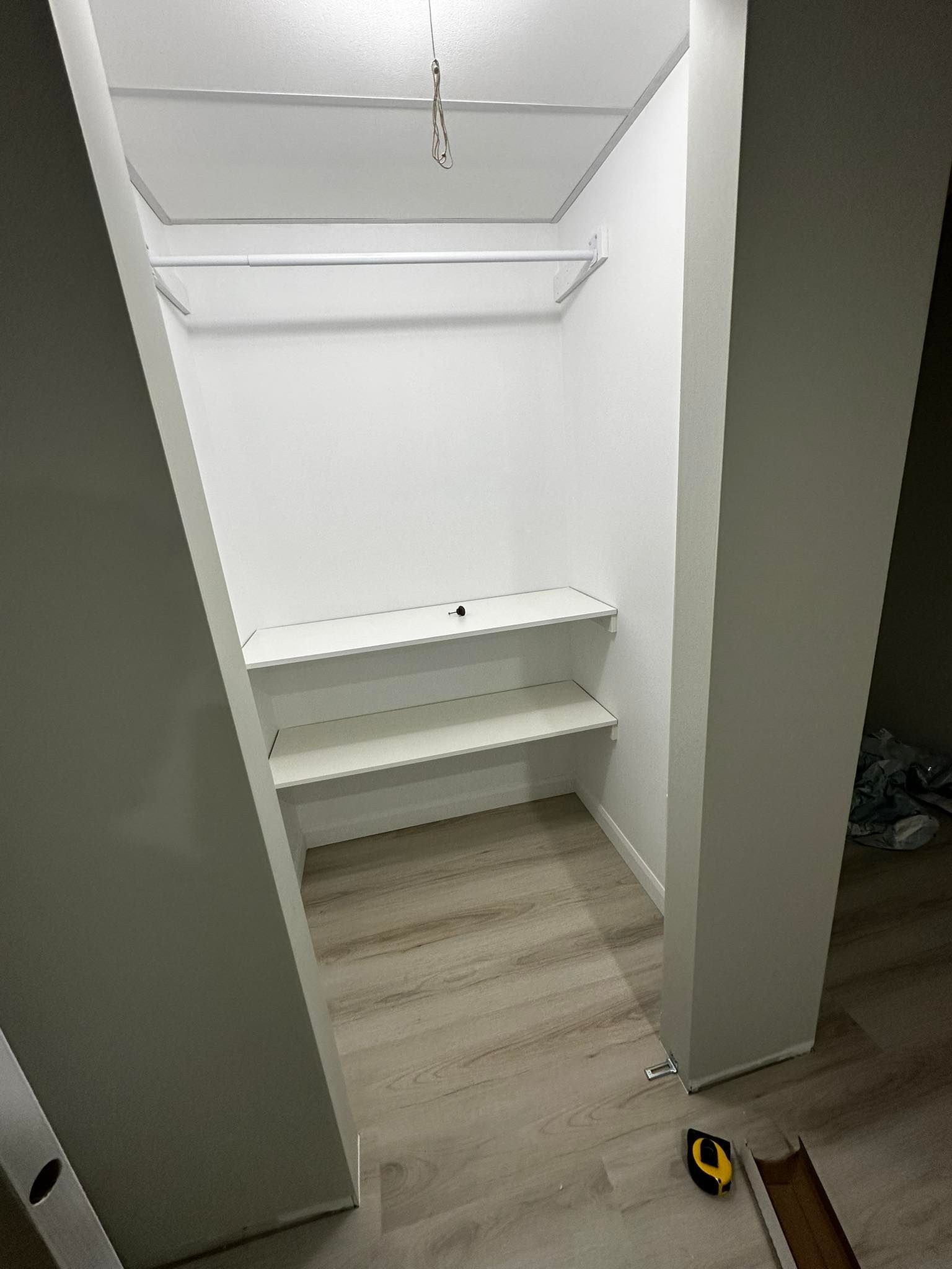 Placard blanc vide avec étagères et tringle, parquet clair, portes du placard ouvertes