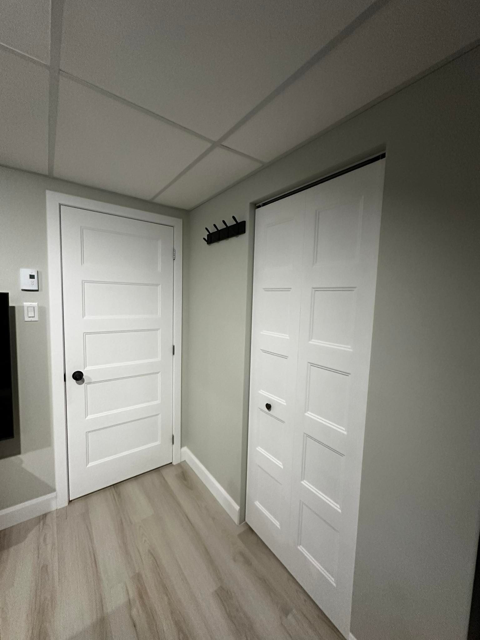 Petit couloir avec une porte blanche, un mur en miroir et des portes de placard dans une pièce grise au sol en bois