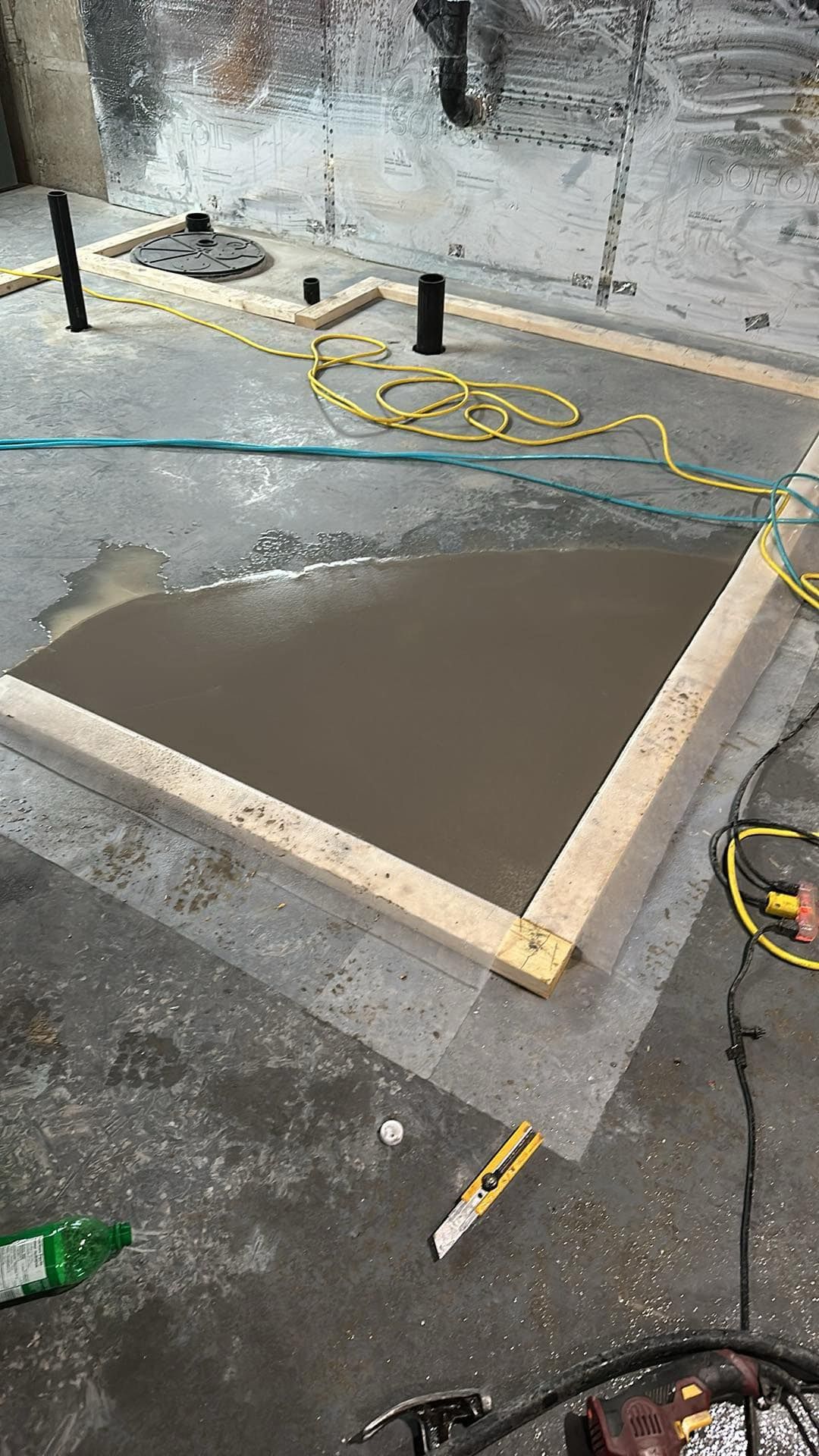 Dalle de béton fraîchement coulée, encadrée de planches de bois, sur un sol de chantier encore humide, avec des câbles jaunes à proximité.