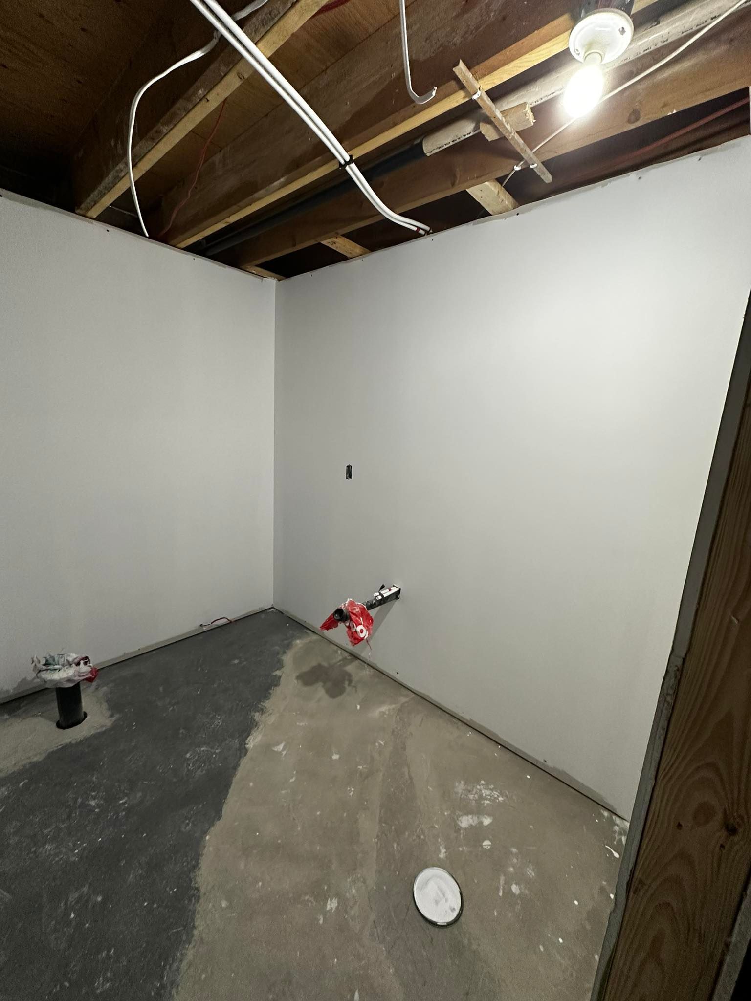 Pièce de sous-sol non aménagée avec murs blancs, poutres apparentes au plafond et matériaux de construction au sol