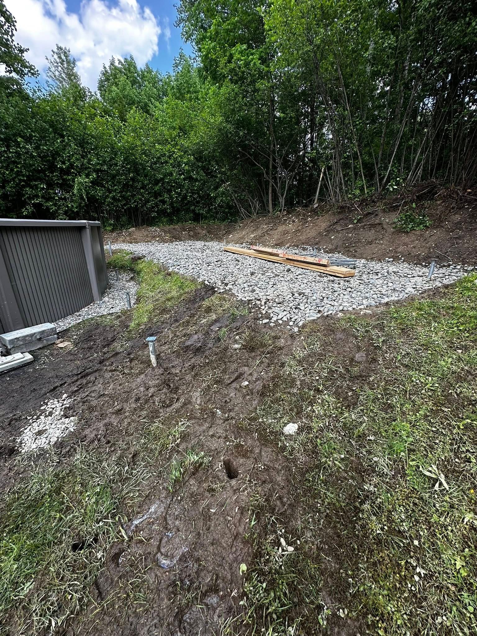 Pente rocheuse et graveleuse jouxtant une structure grise, avec des arbres verts en arrière-plan.