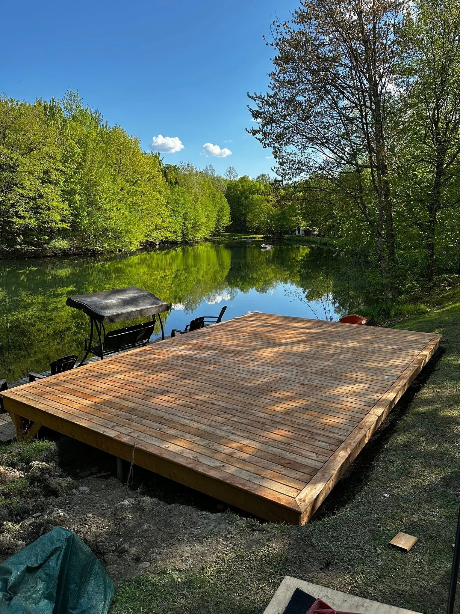 Un quai en bois au bord d'une rivière calme, entouré d'arbres verdoyants sous un ciel bleu.