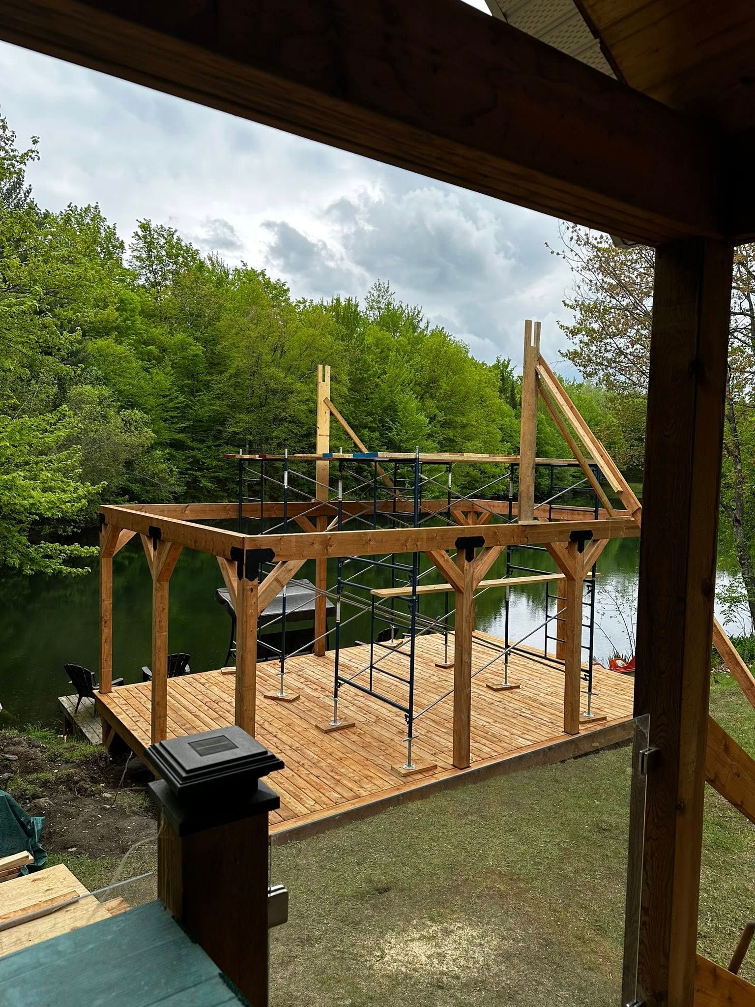 Structure de jeux en bois avec filet de corde et bac à sable, vue depuis une véranda, entourée d'arbres.
