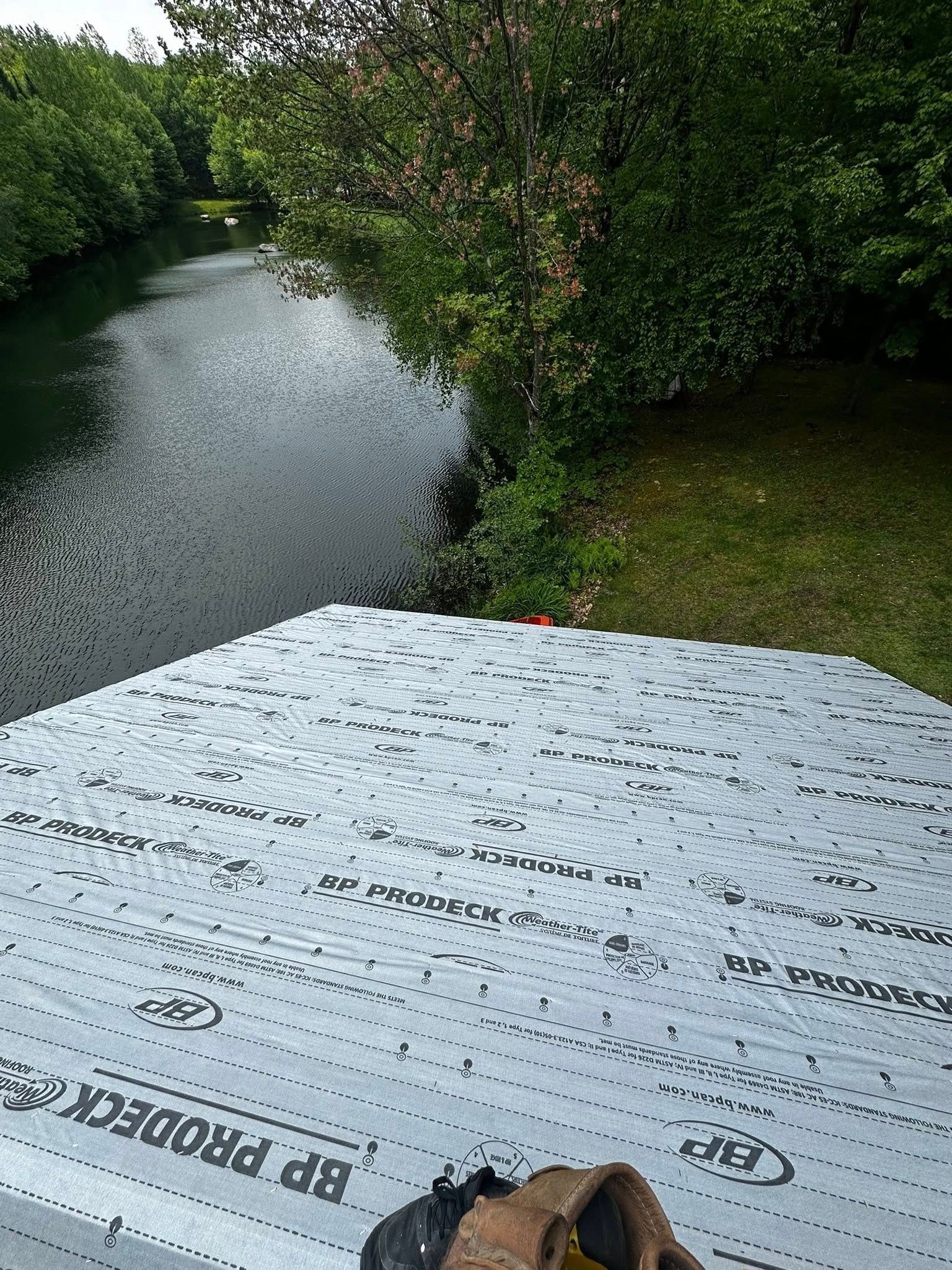 Ruisseau brumeux bordé d'arbres verdoyants, vu depuis une plateforme humide, avec une tasse au premier plan.