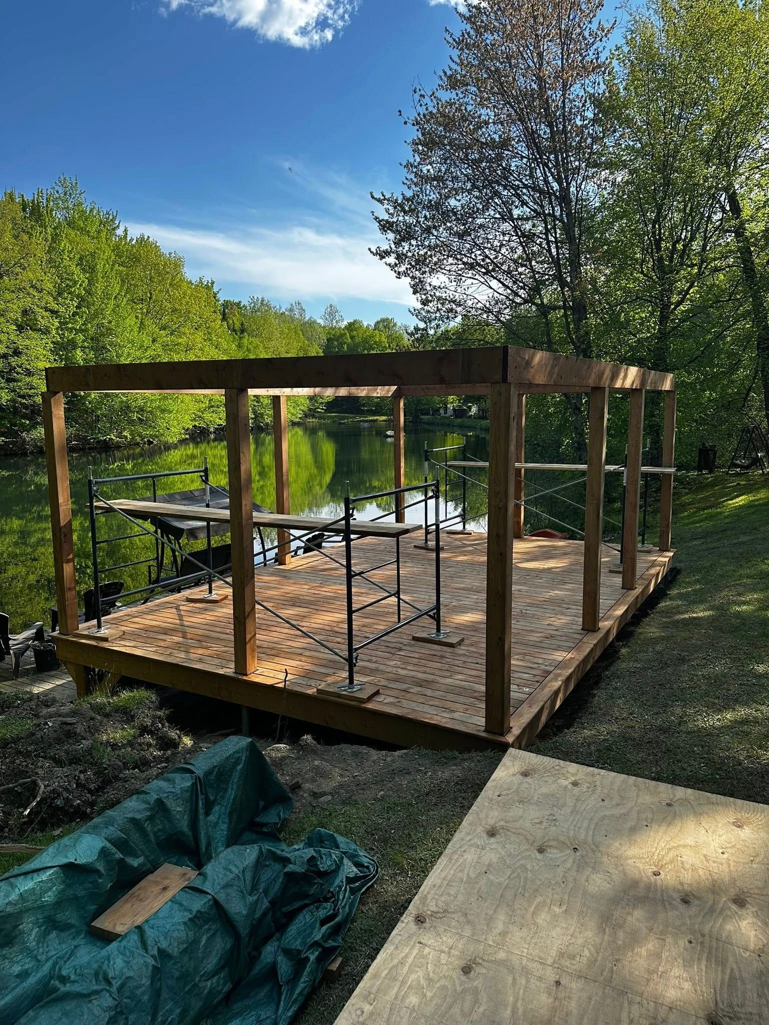 Construction d'une structure de terrasse en bois dans un jardin arboré, avec outils et matériaux à proximité.