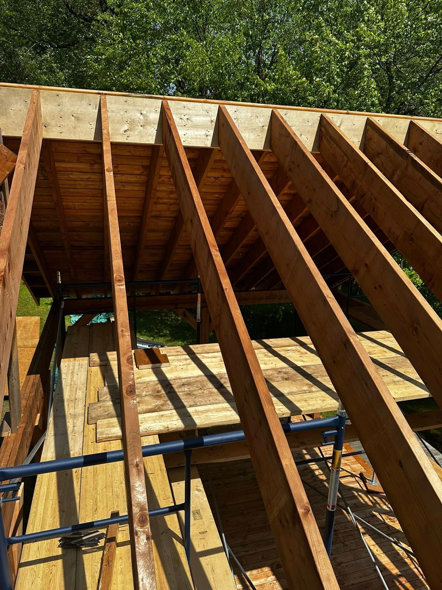 Charpente de toit en bois en construction, avec chevrons apparents et échafaudages sur fond vert.