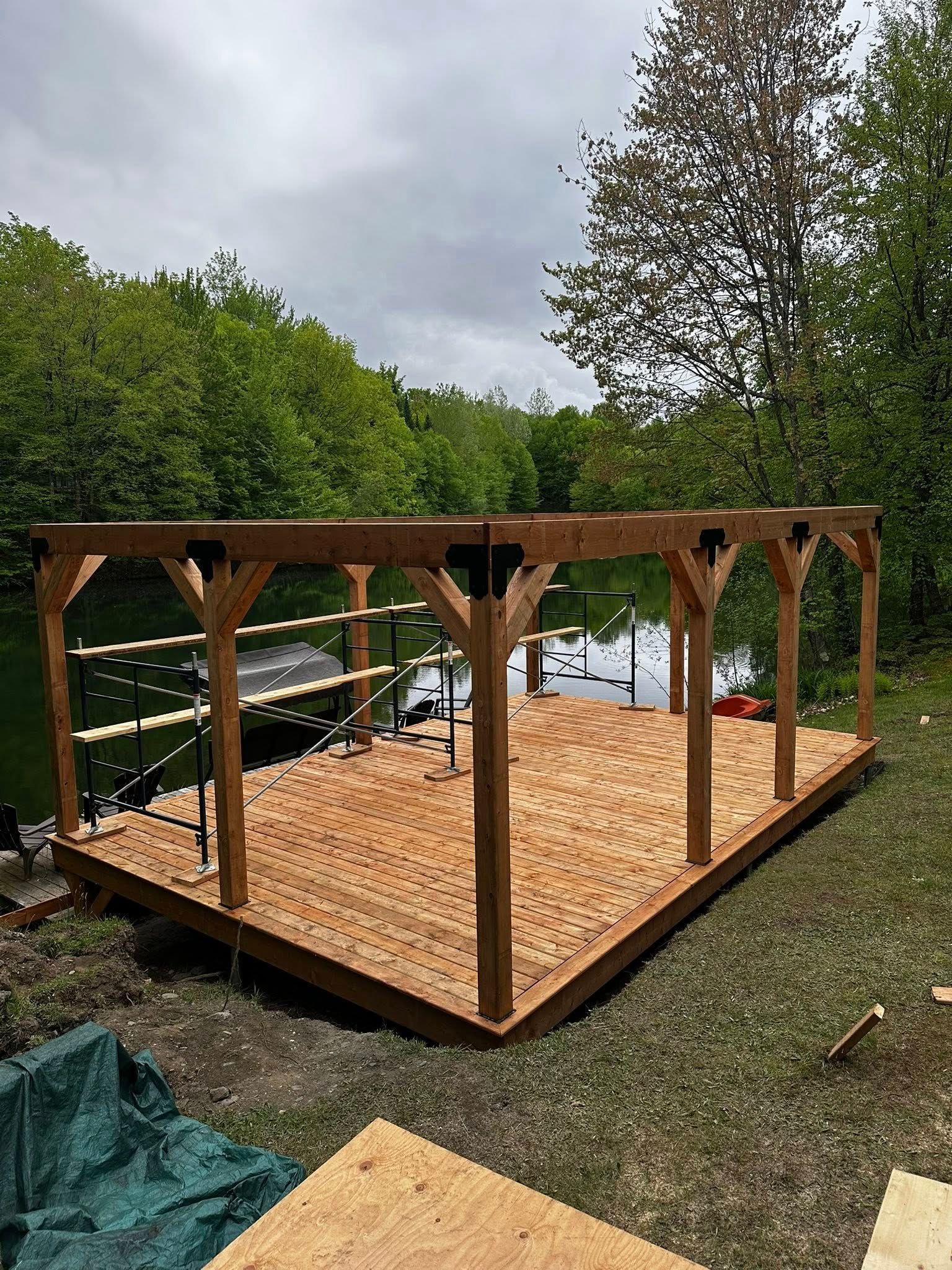 La structure en bois de la terrasse, avec ses poteaux, est en construction près d'un étang et d'arbres.