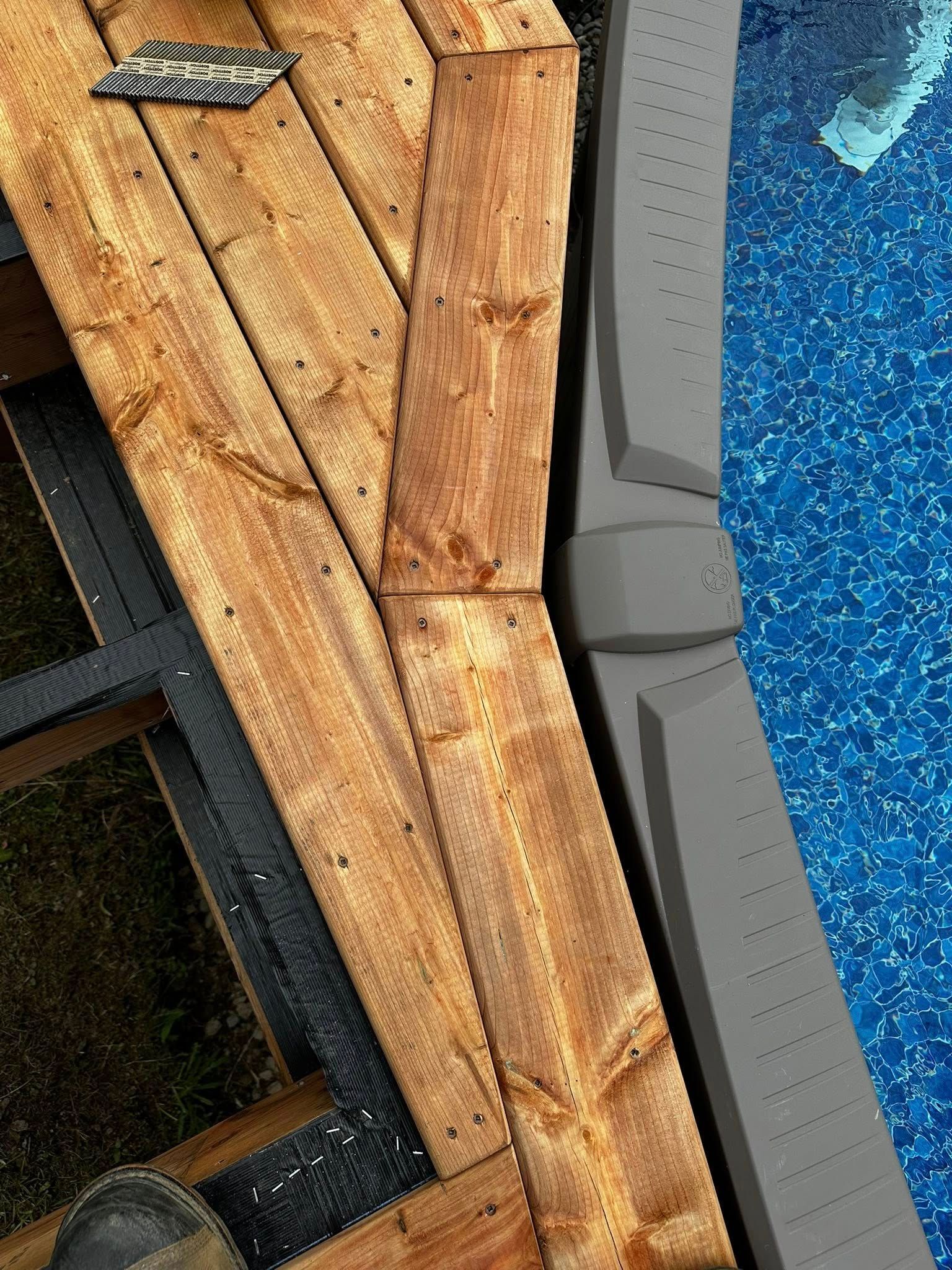 Terrasse de piscine en bois bordant une piscine grise et une eau bleue, avec une rampe d'échelle visible.