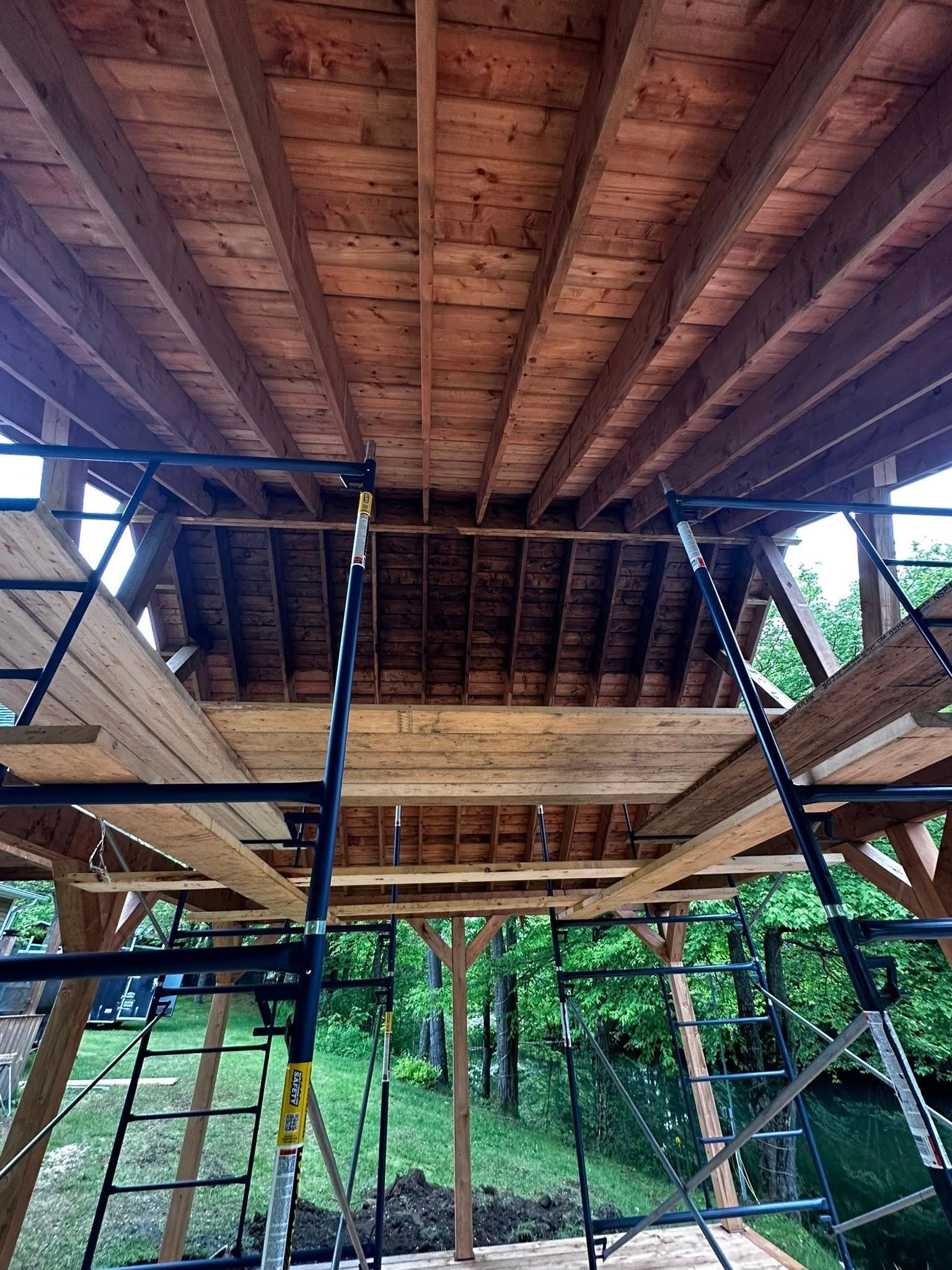Terrasse en bois en construction, avec échafaudages et poutres de toit apparentes au milieu des arbres