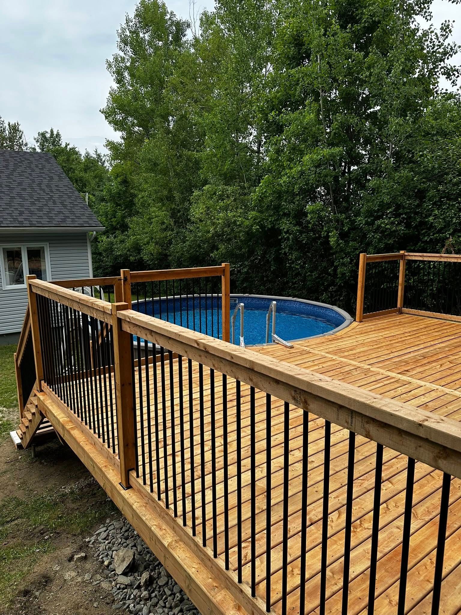 Terrasse en bois avec rambarde noire à côté d'une piscine hors sol dans un jardin