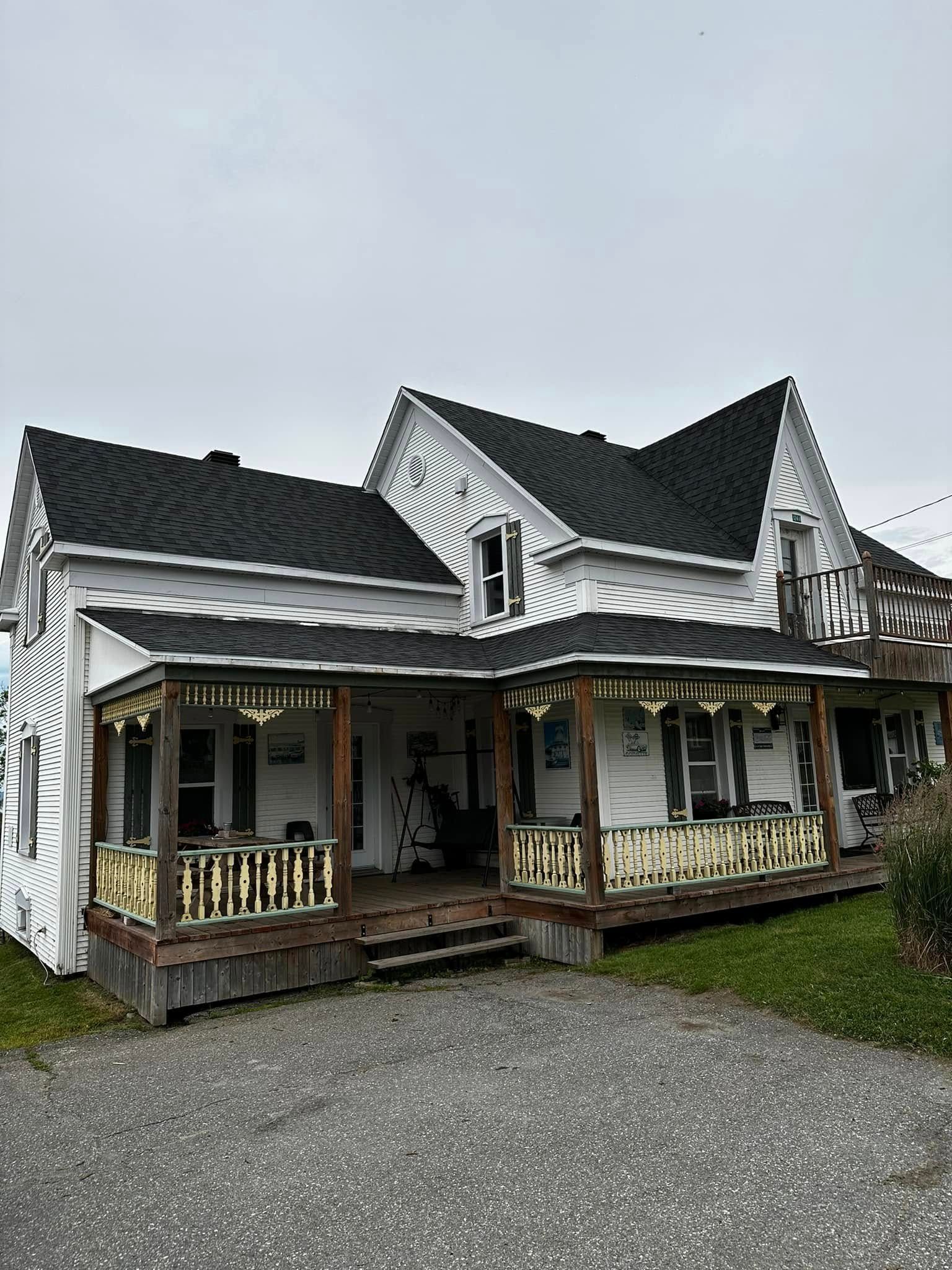 Maison blanche fantaisiste avec toit noir, ornements travaillés et porches couverts donnant sur une allée de gravier