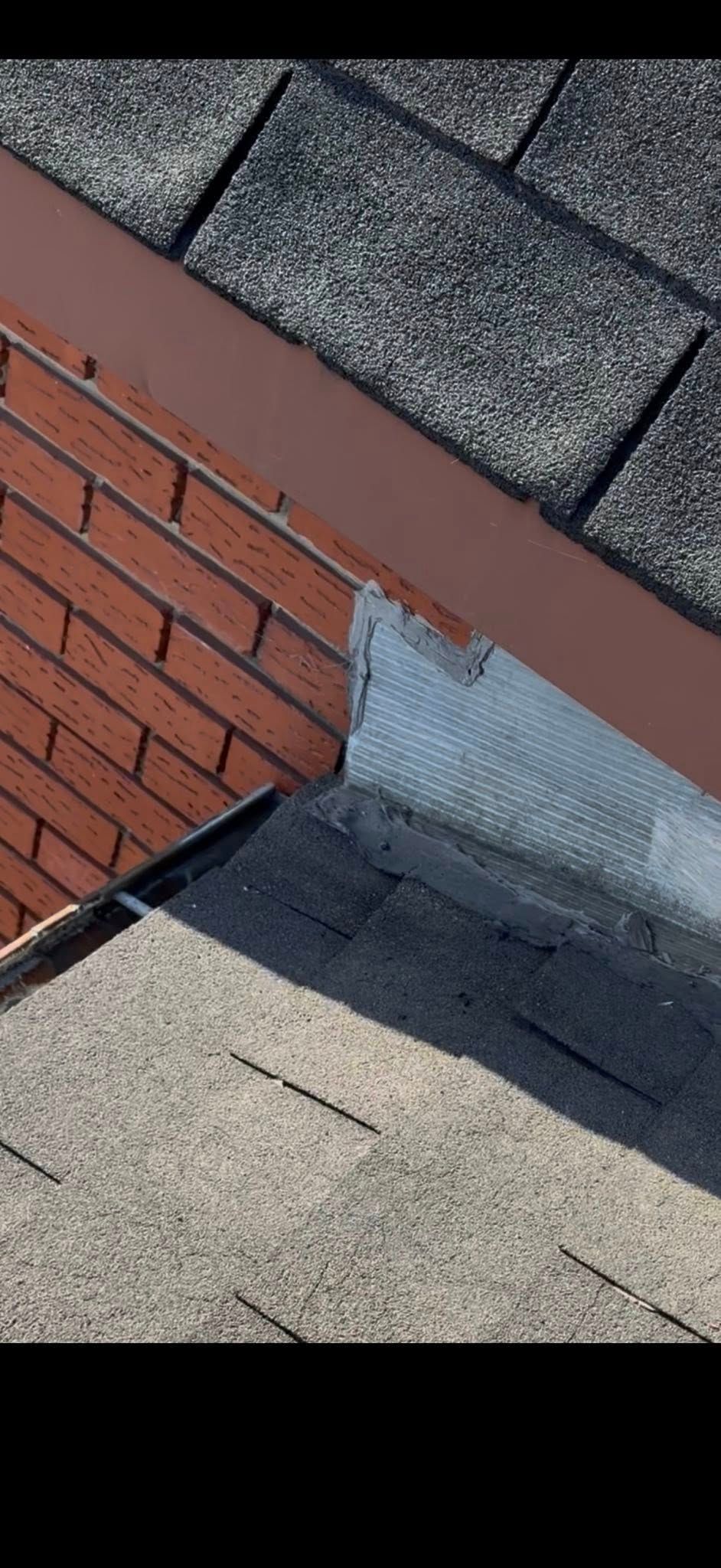 Gros plan sur un angle de toit avec un mur en briques rouges, des bardeaux foncés et des solins métalliques.