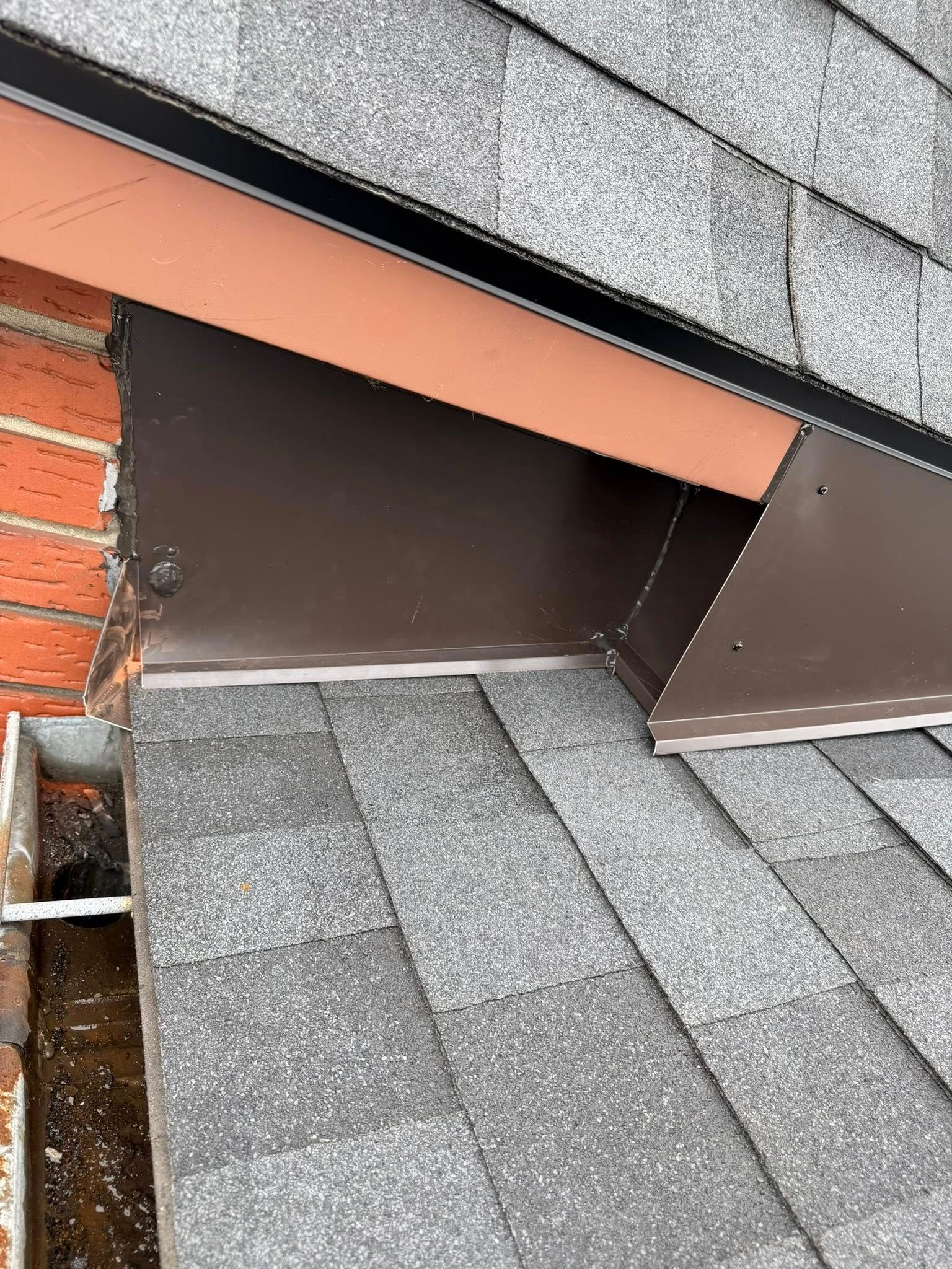 Gros plan sur une ouverture de ventilation de toit avec des bardeaux gris et des solins apparents près d'un mur de briques