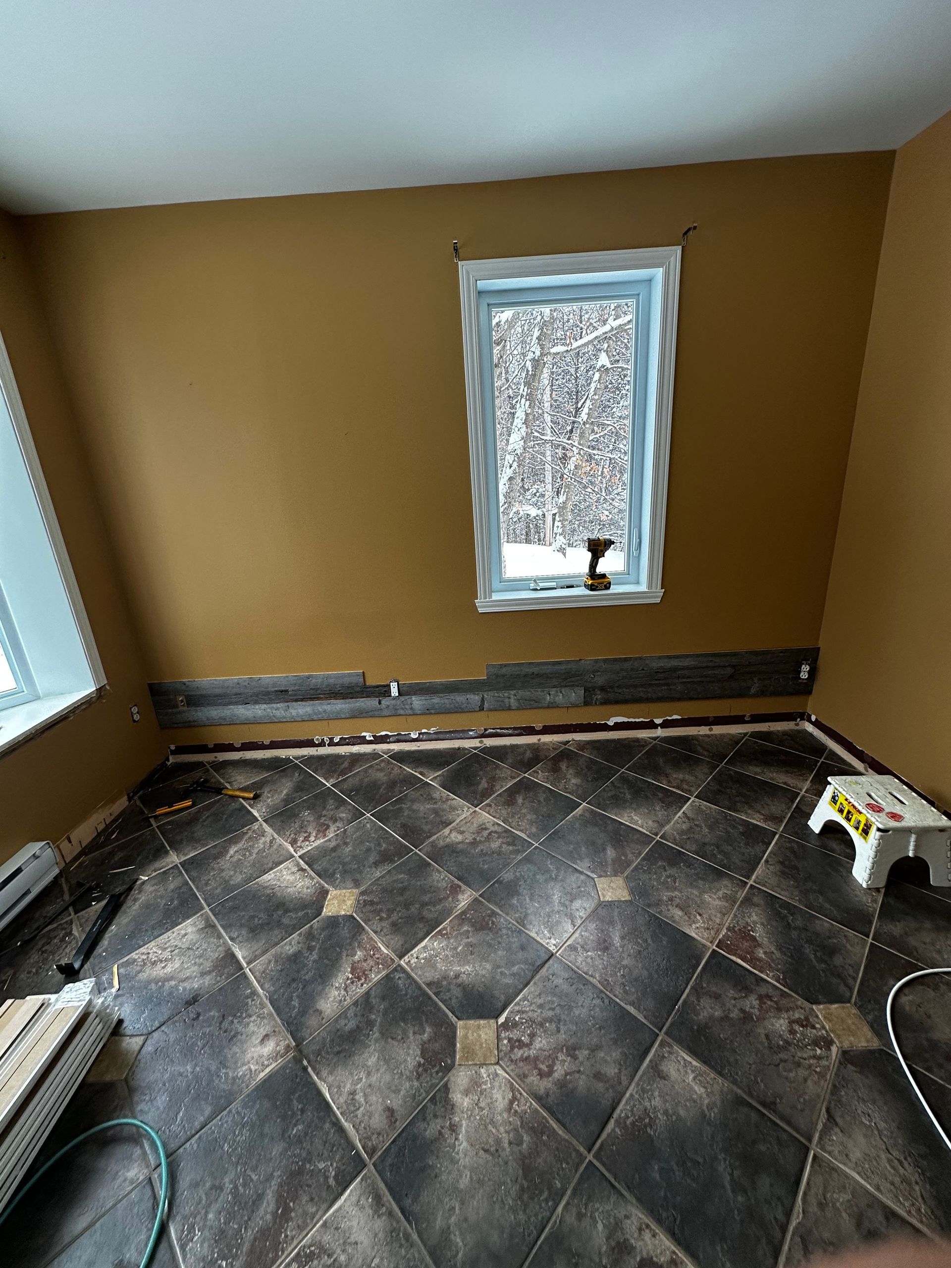Pièce vide aux murs marron, au sol carrelé foncé et dotée de deux fenêtres, en cours de rénovation.