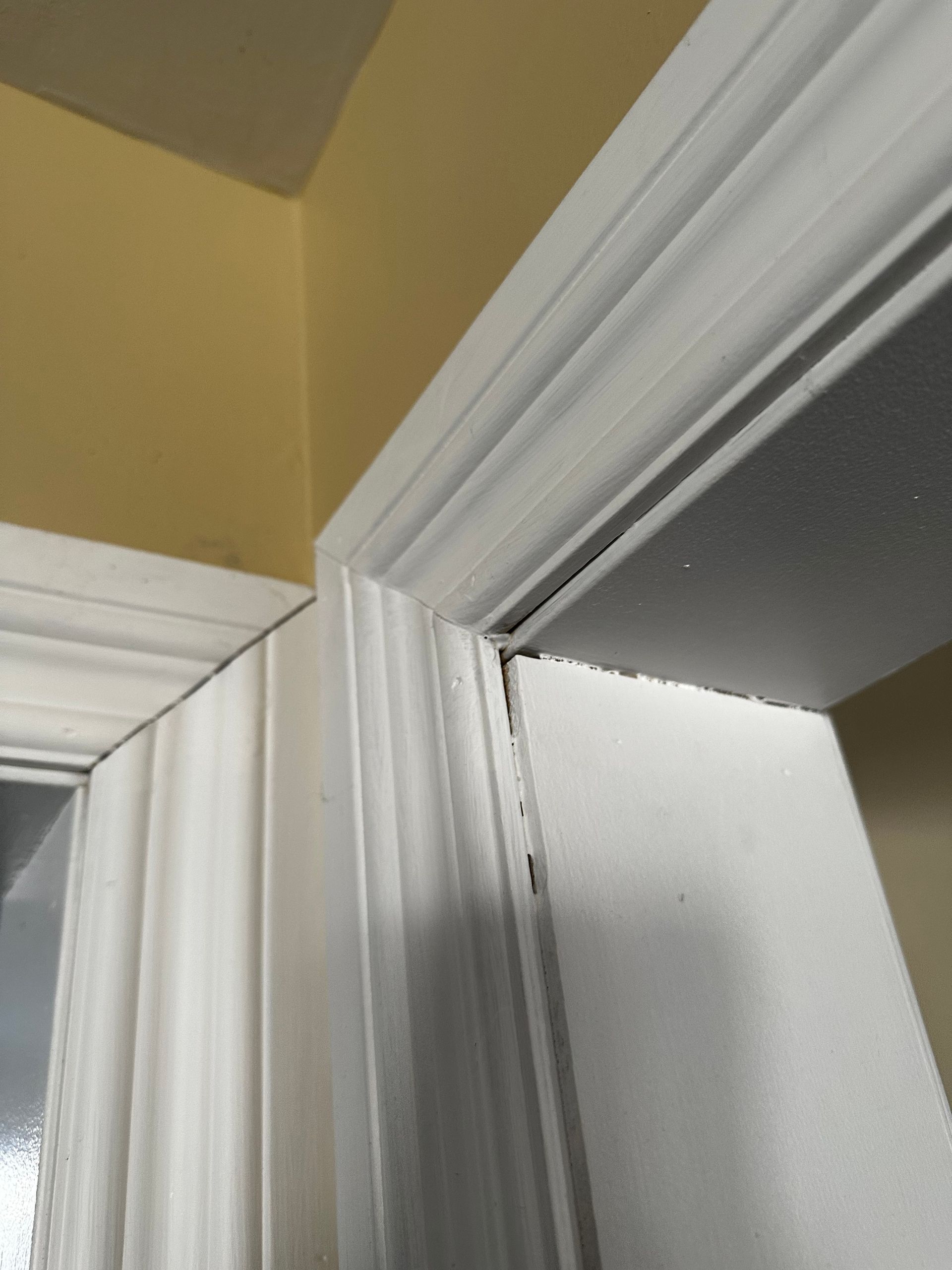 Gros plan sur un coin d'encadrement de porte blanc se détachant sur un mur jaune et un plafond gris.