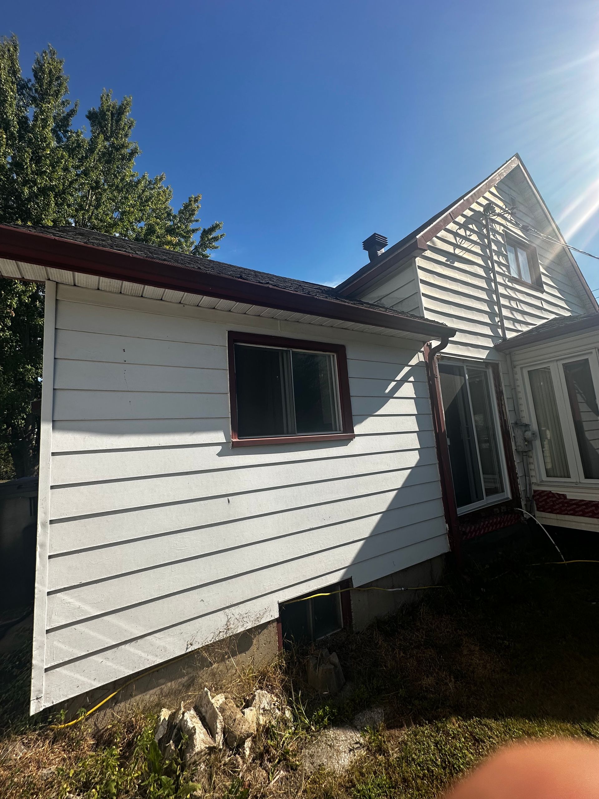 Extérieur d'une maison blanche avec un toit en pente, une fenêtre et un petit porche sous un ciel bleu clair
