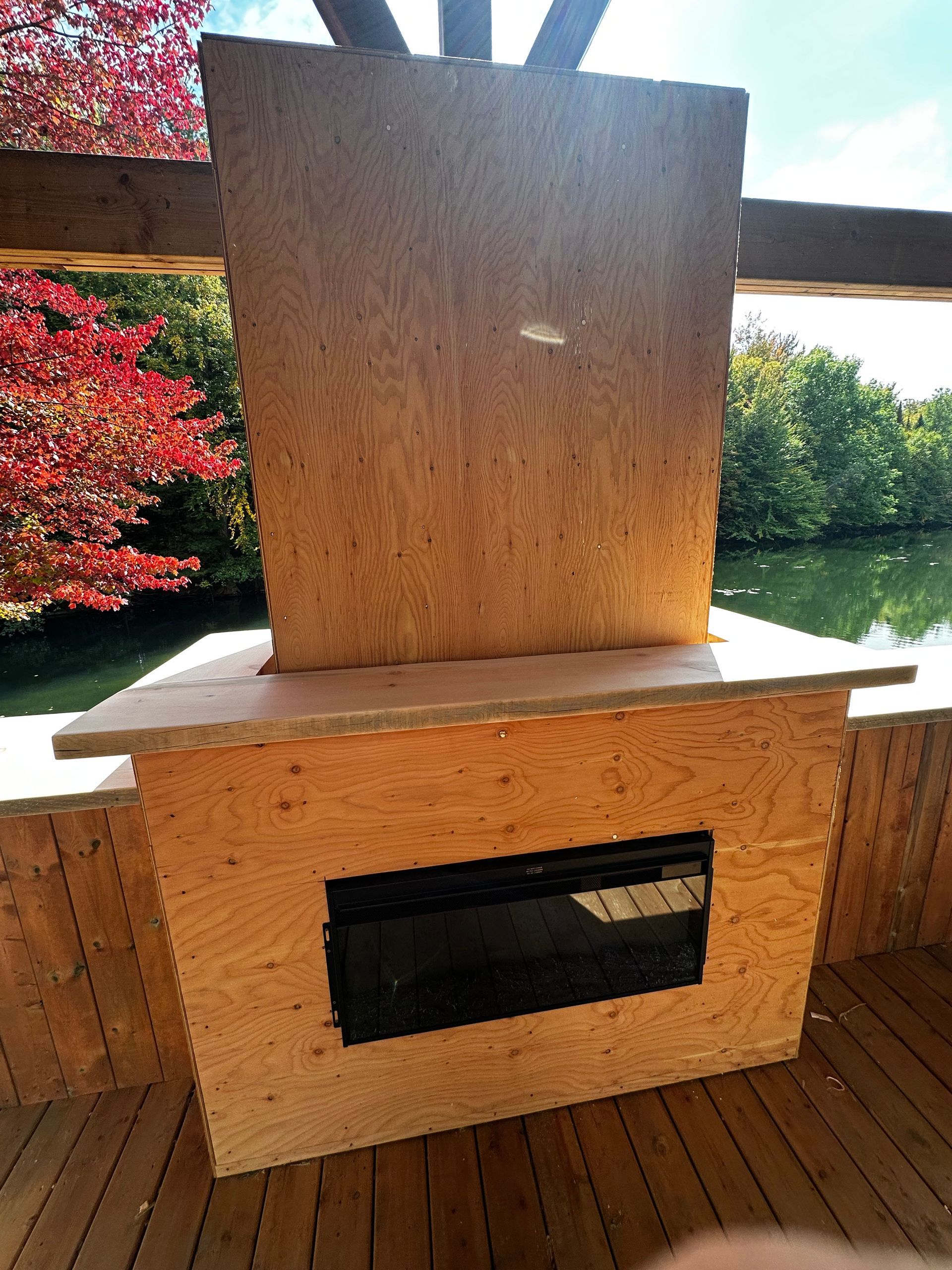 Cheminée à bois sur une terrasse en bois donnant sur un lac et des arbres aux feuilles rouges