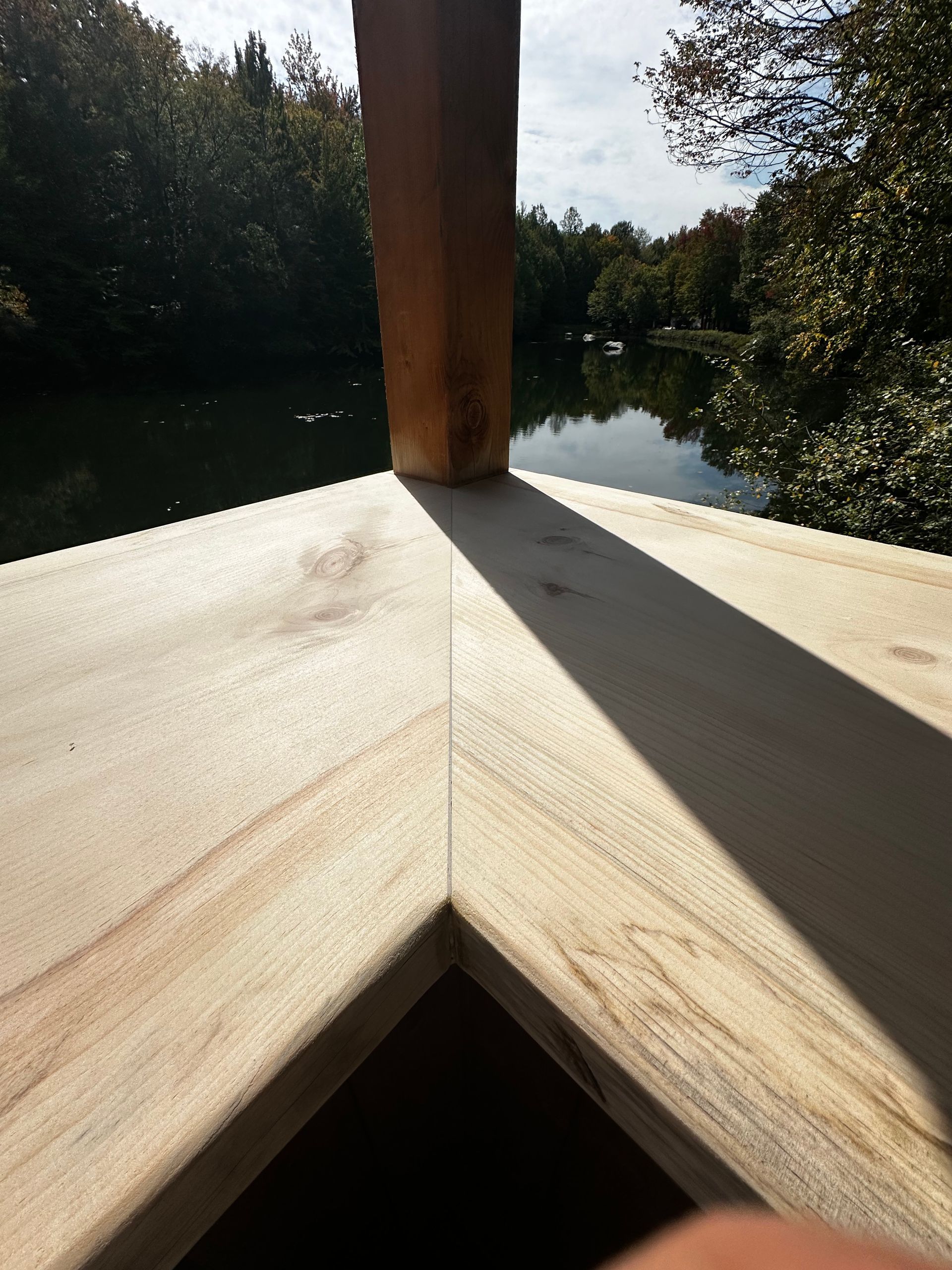 Coin de terrasse en bois donnant sur un lac calme où se reflètent les arbres.