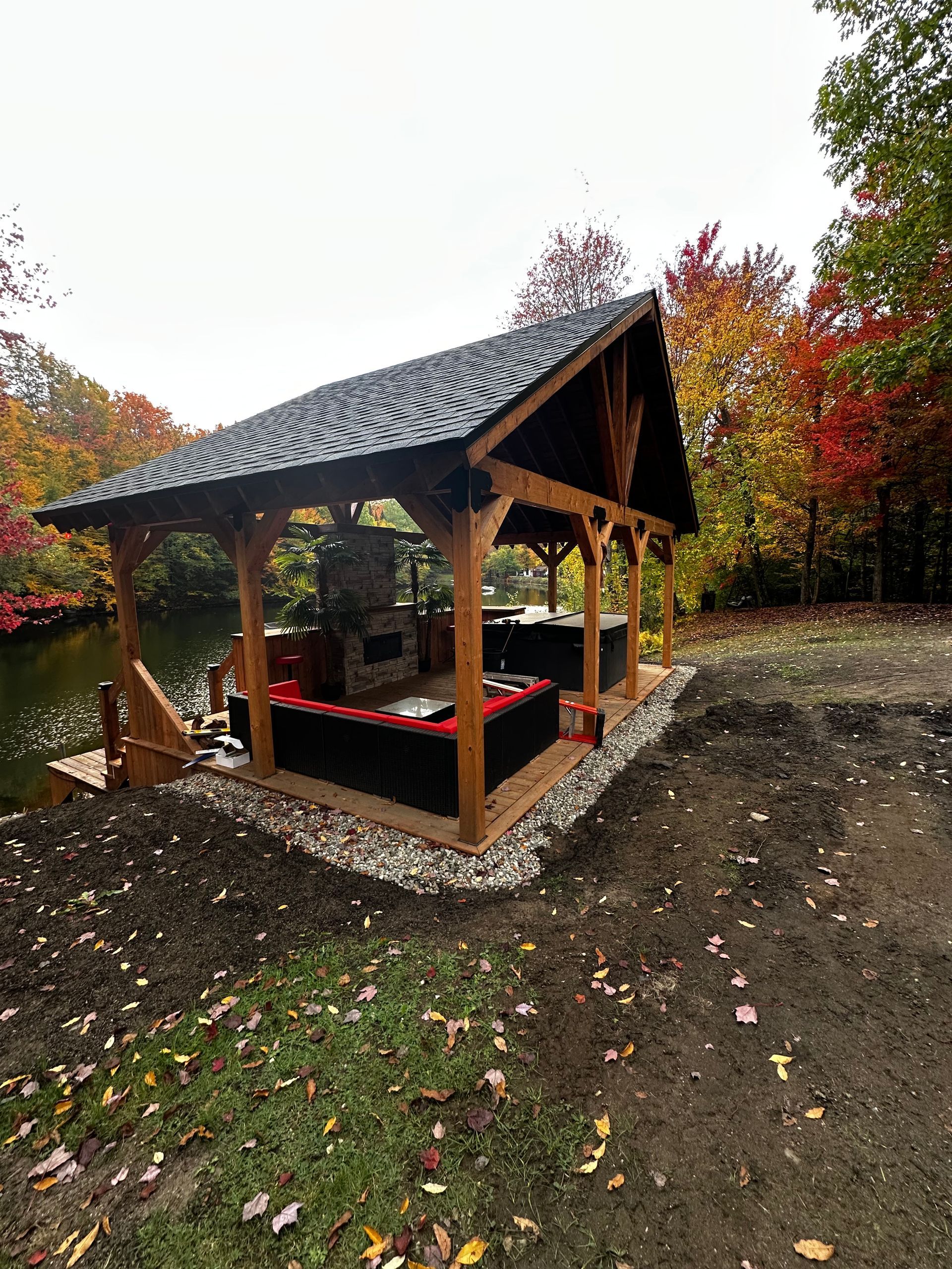 Pavillon en bois au toit de bardeaux sombres, situé au bord d'un chemin de terre et entouré d'arbres aux teintes automnales.