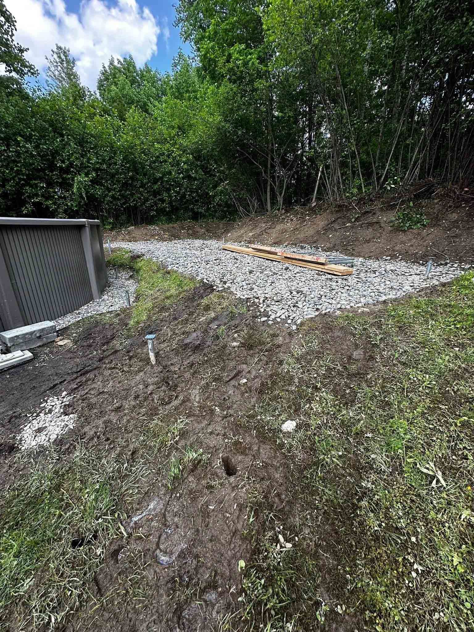 Pente rocheuse et graveleuse jouxtant une structure grise, avec des arbres verts en arrière-plan.